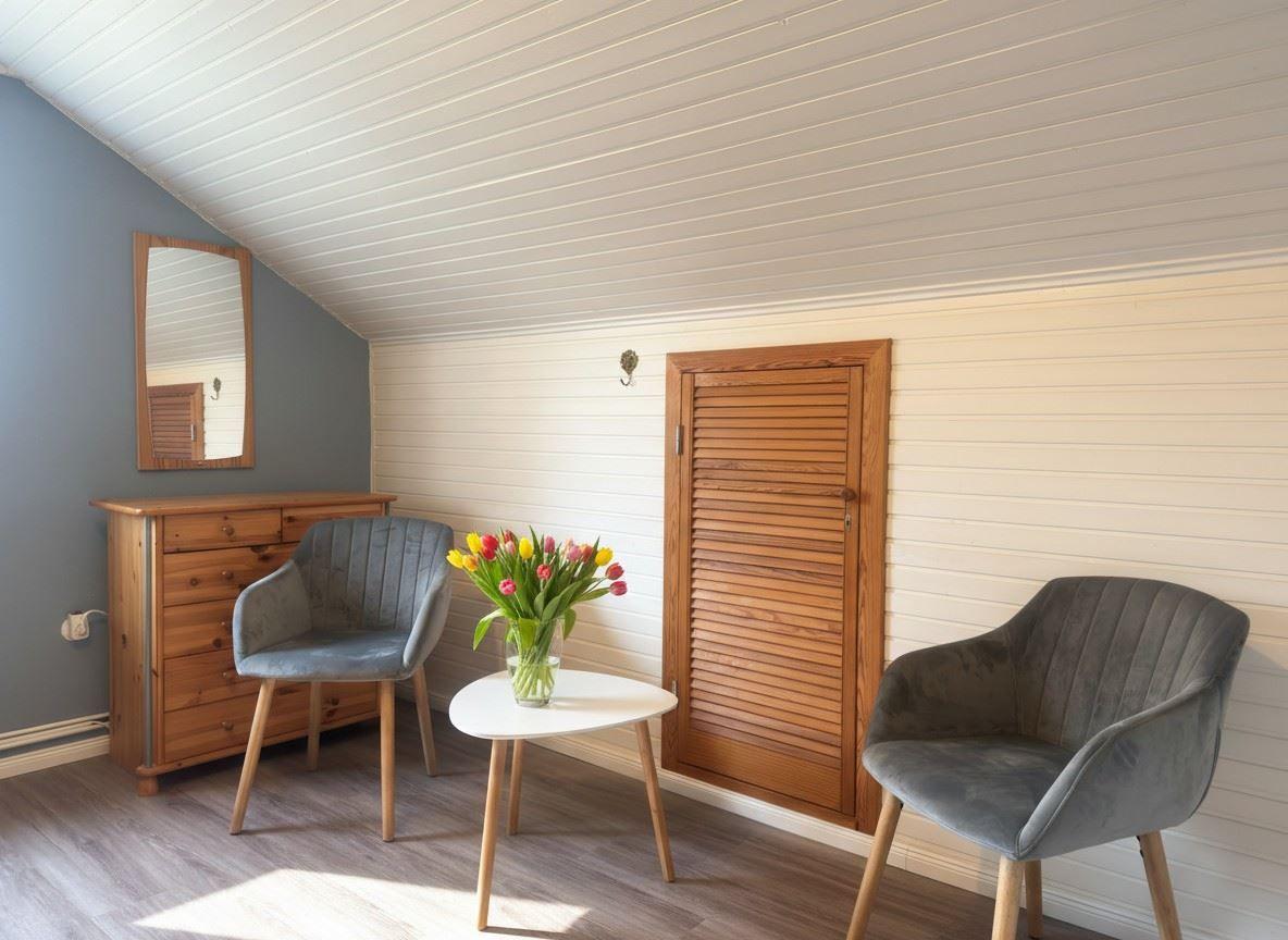Zimmer mit zwei Stühlen, Tisch und Blumen. Holzwand und Dachschräge.