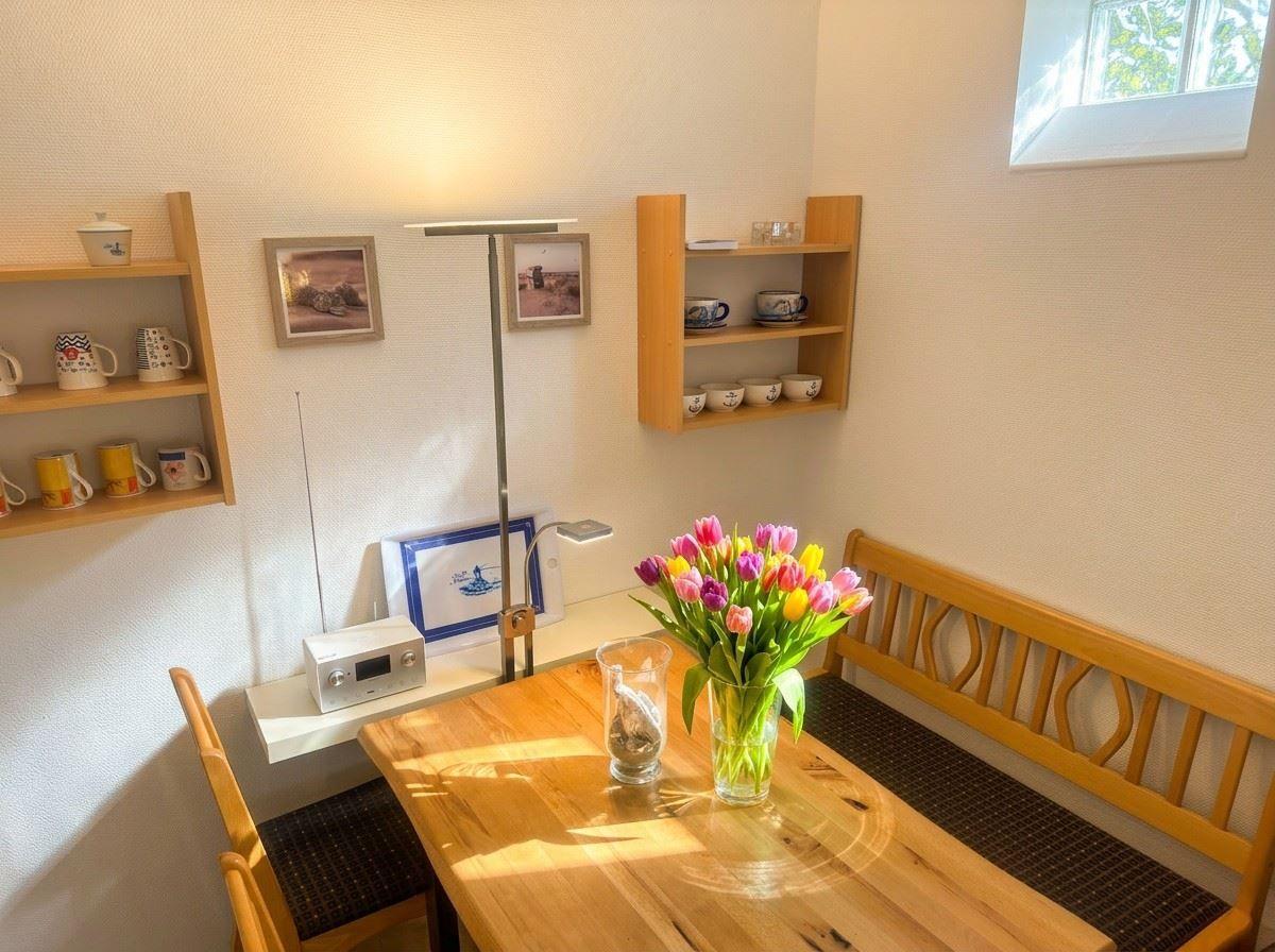 Holztisch mit Blumen, Sitzbank und Wandregale mit Tassen.