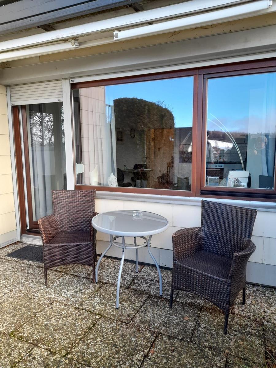 Terrasse mit zwei Stühlen und Tisch vor Fenster und Glastür
