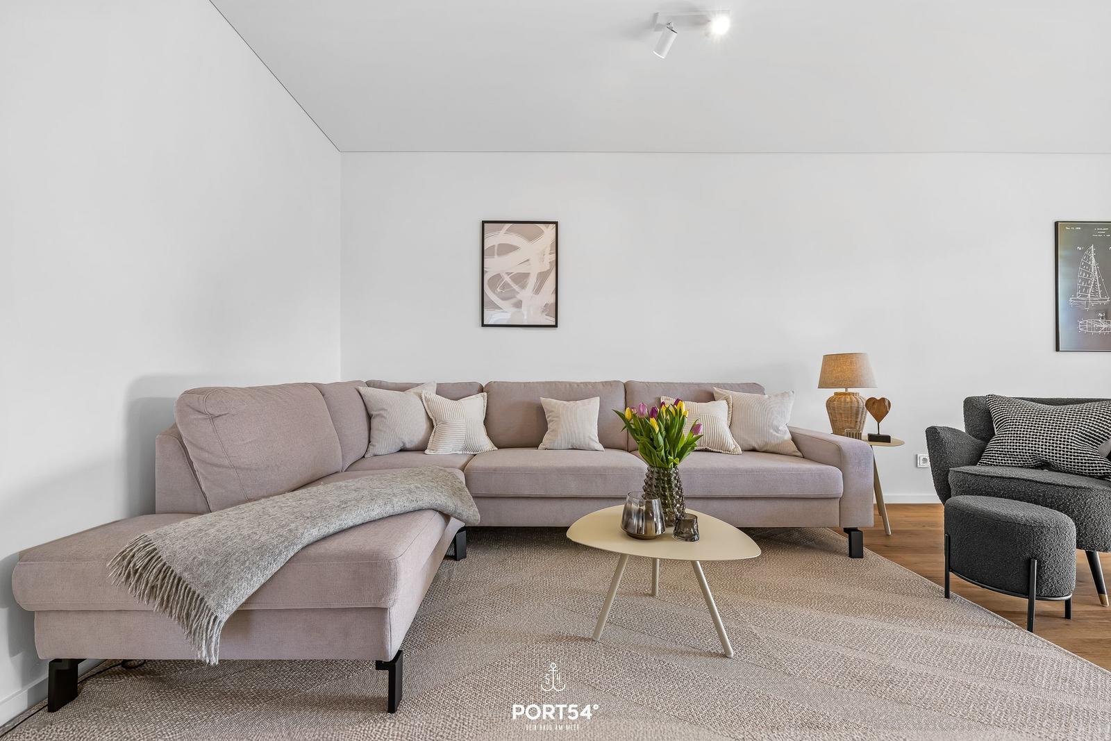 Ein Wohnzimmer mit einem hellen Sofa, einem runden Tisch und einem Beistelltisch.