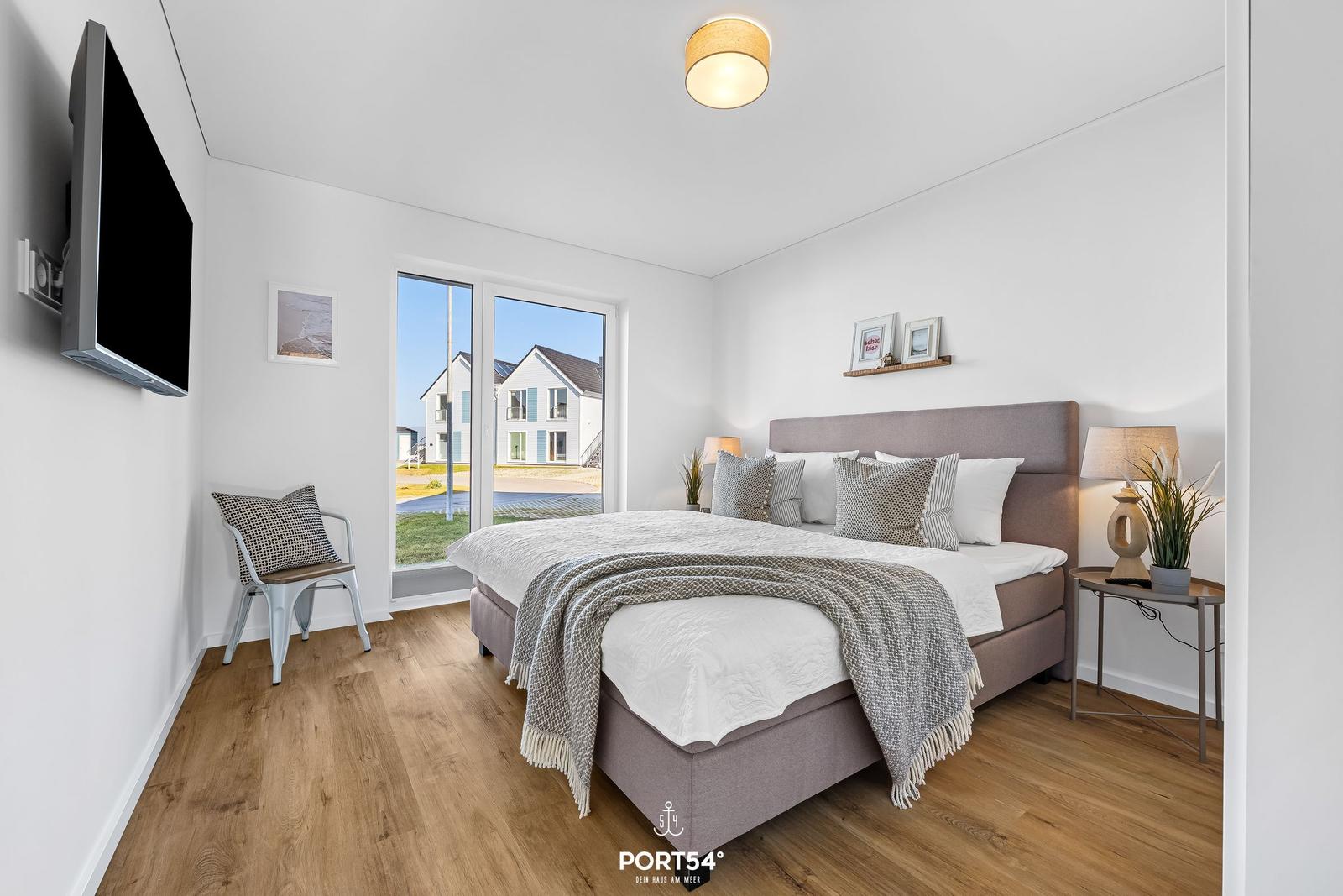 Schlafzimmer mit Bett, TV und Fensterblick auf Haus