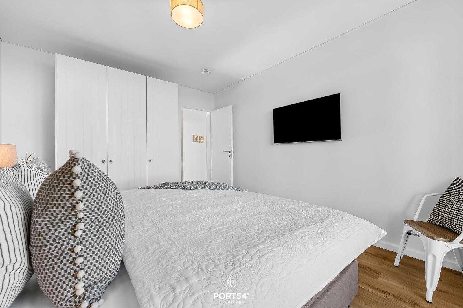 Schlafzimmer mit Bett, Kleiderschrank, Fernseher und Stuhl.