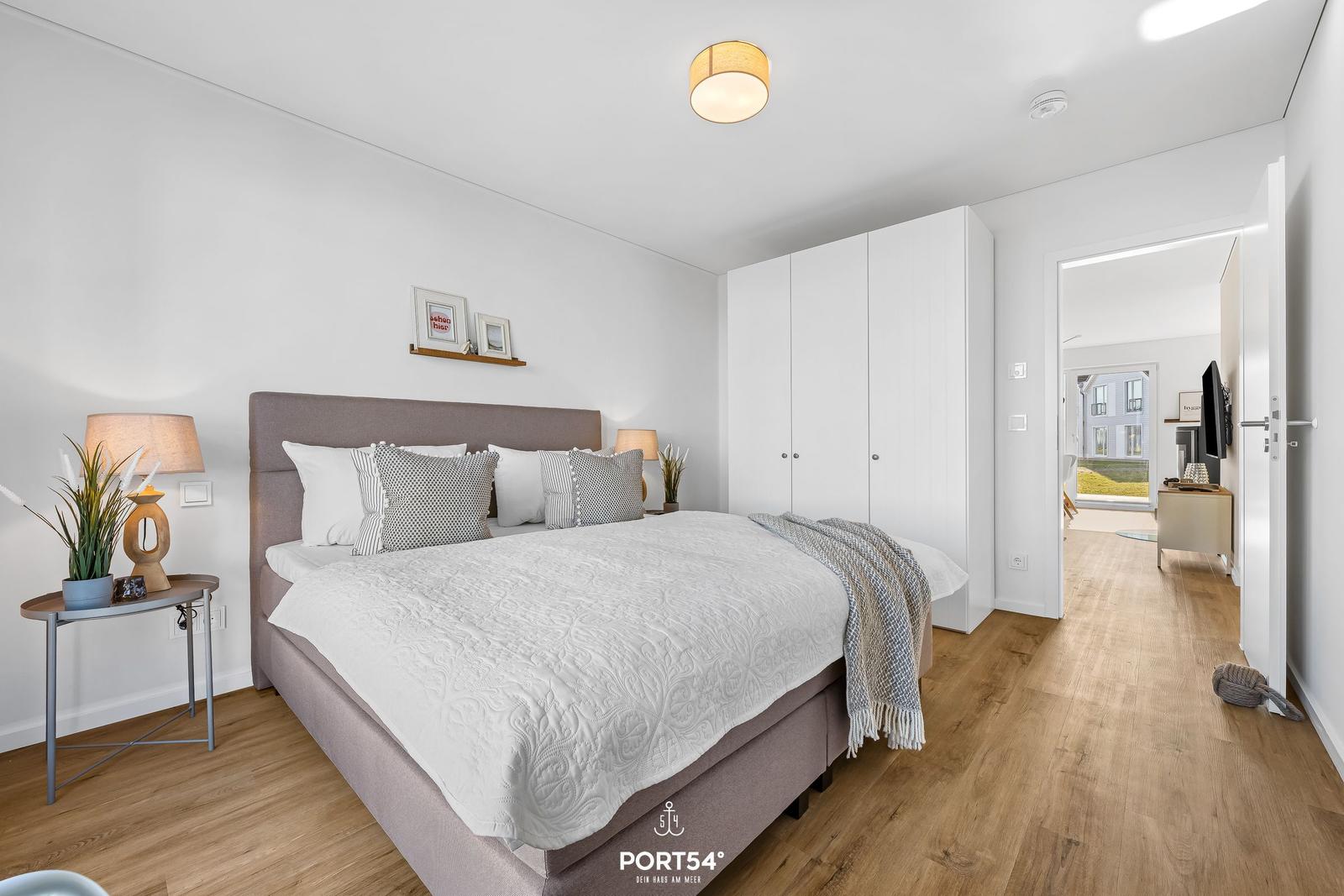 Schlafzimmer mit Bett, Kleiderschrank und Holzboden. Durchgang zum Wohnbereich.