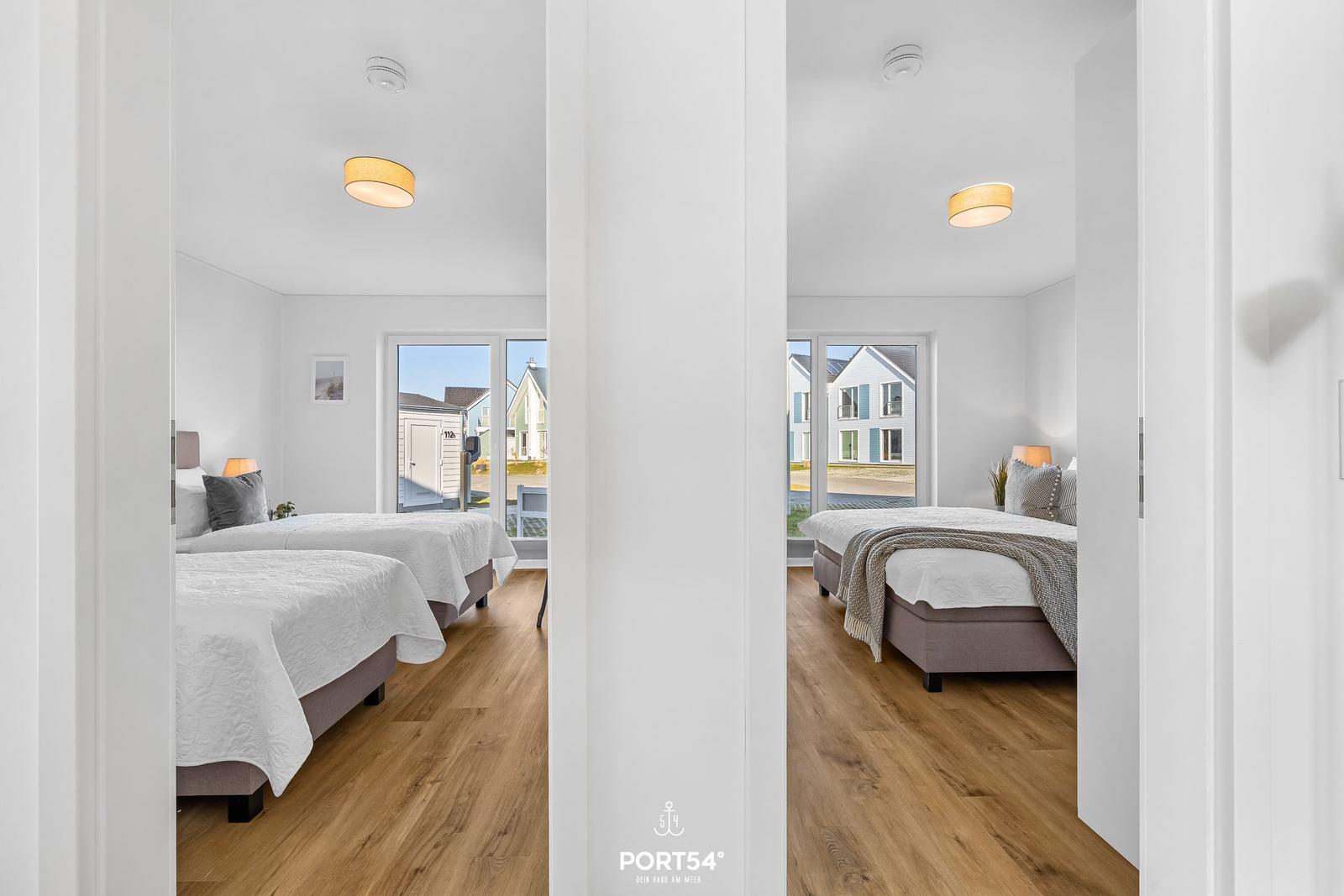Zwei Schlafzimmer mit Betten, Holzboden und Fenstern zum Außenbereich.