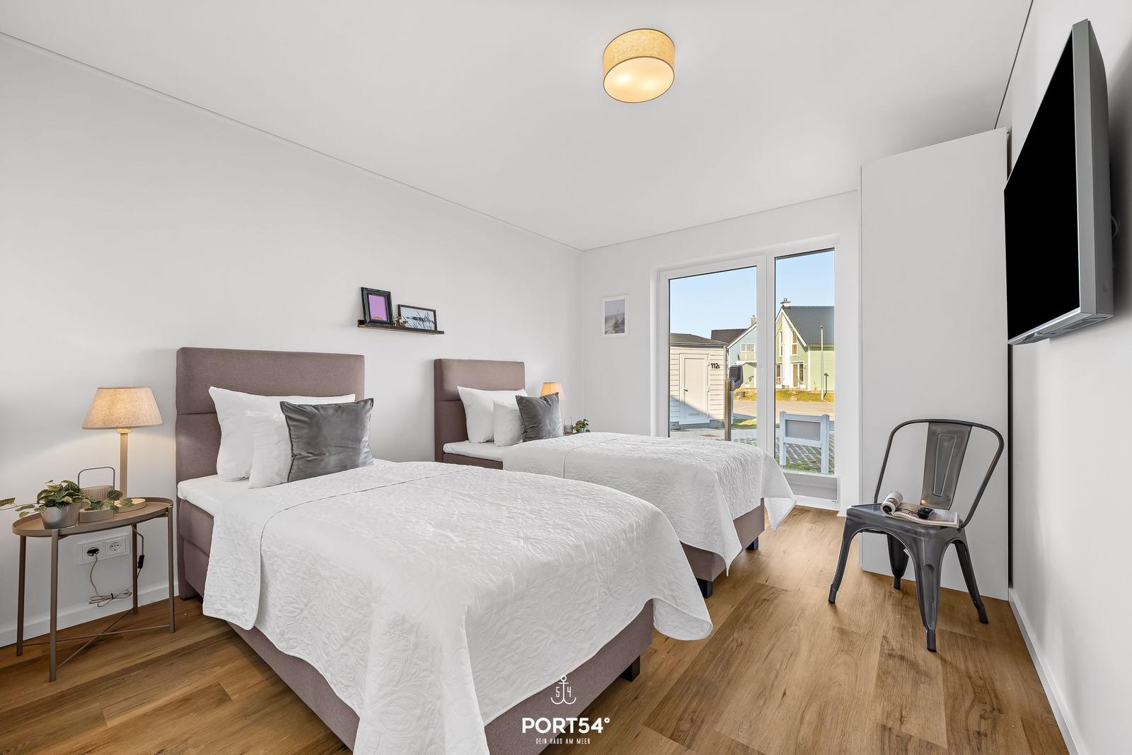 Zwei Betten, Holzboden, Fensterblick, Wand-TV und Stuhl im Zimmer.