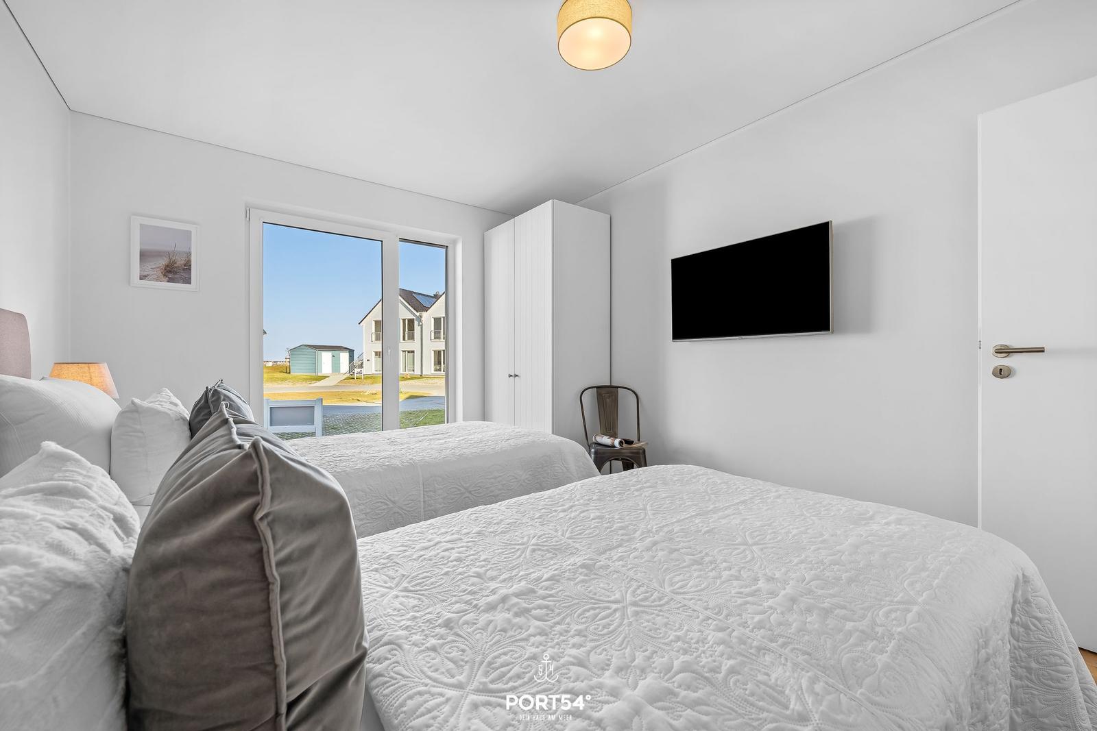 Zwei Betten mit weißen Bezügen, Fernseher und Fenster mit Blick auf Außenbereich.
