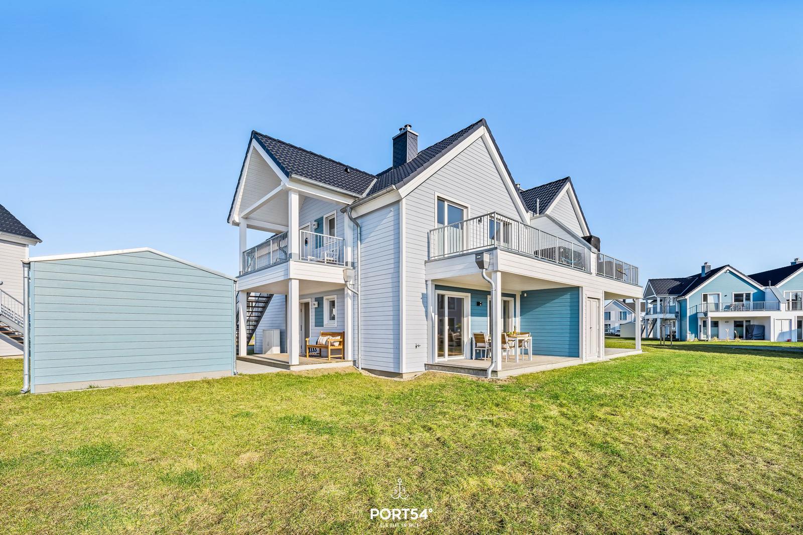 Modernes Haus mit Balkon und Terrasse auf grünem Grundstück.