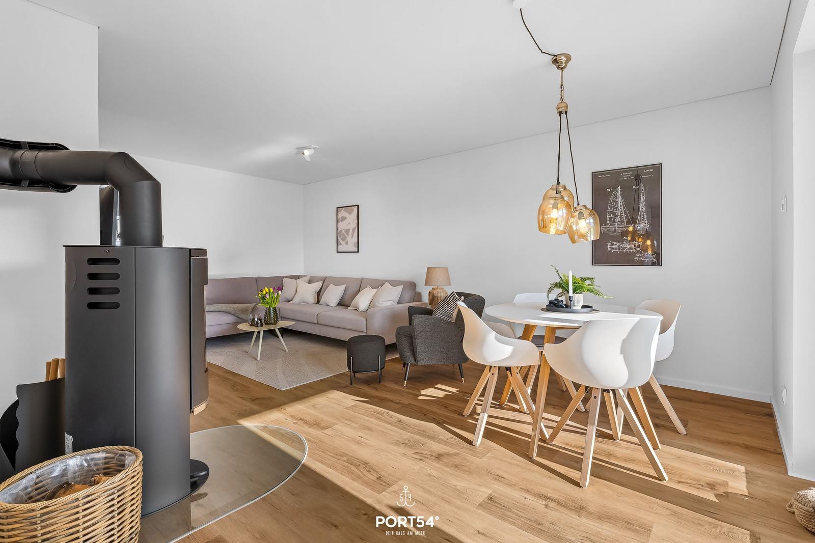 Wohn- und Essbereich mit Holzboden, Sofa, Esstisch und Kaminofen.