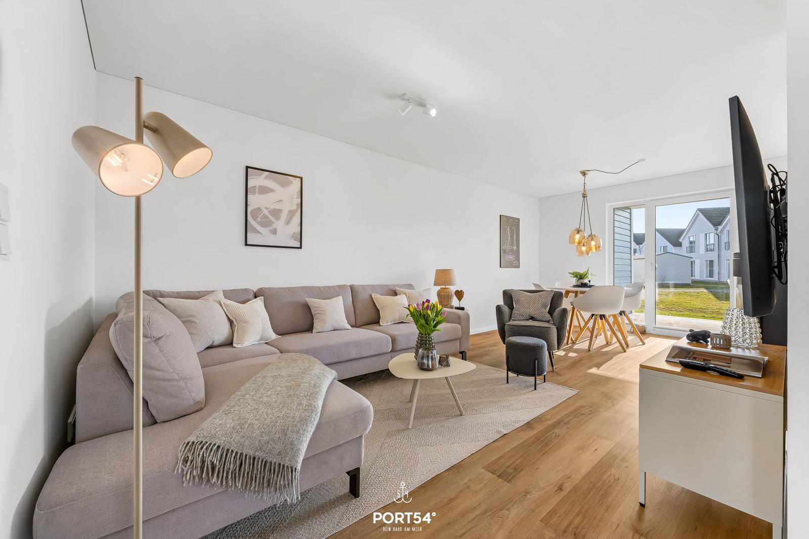 Wohnzimmer mit Sofa, Couchtisch und Fernseher. Esstisch mit Stühlen und Fensterblick.