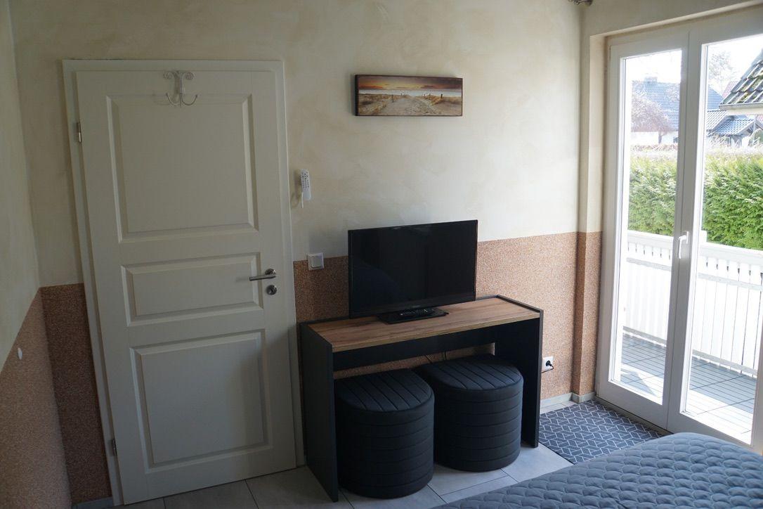 Zimmer mit TV, Stühlen und Balkontür. Wandbild und Tür sichtbar.