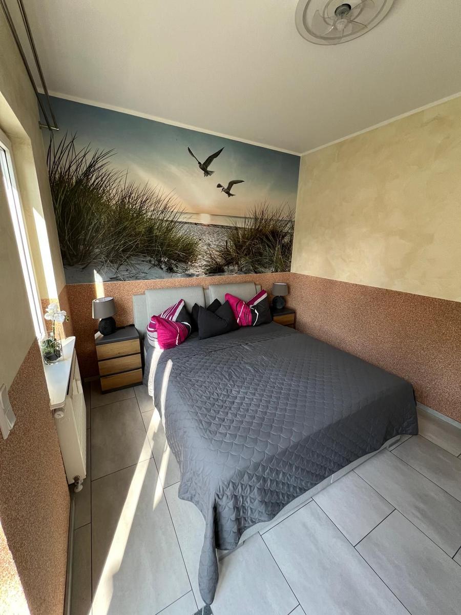 Schlafzimmer mit Bett, Nachttischen und Wandbild mit Strandmotiv.