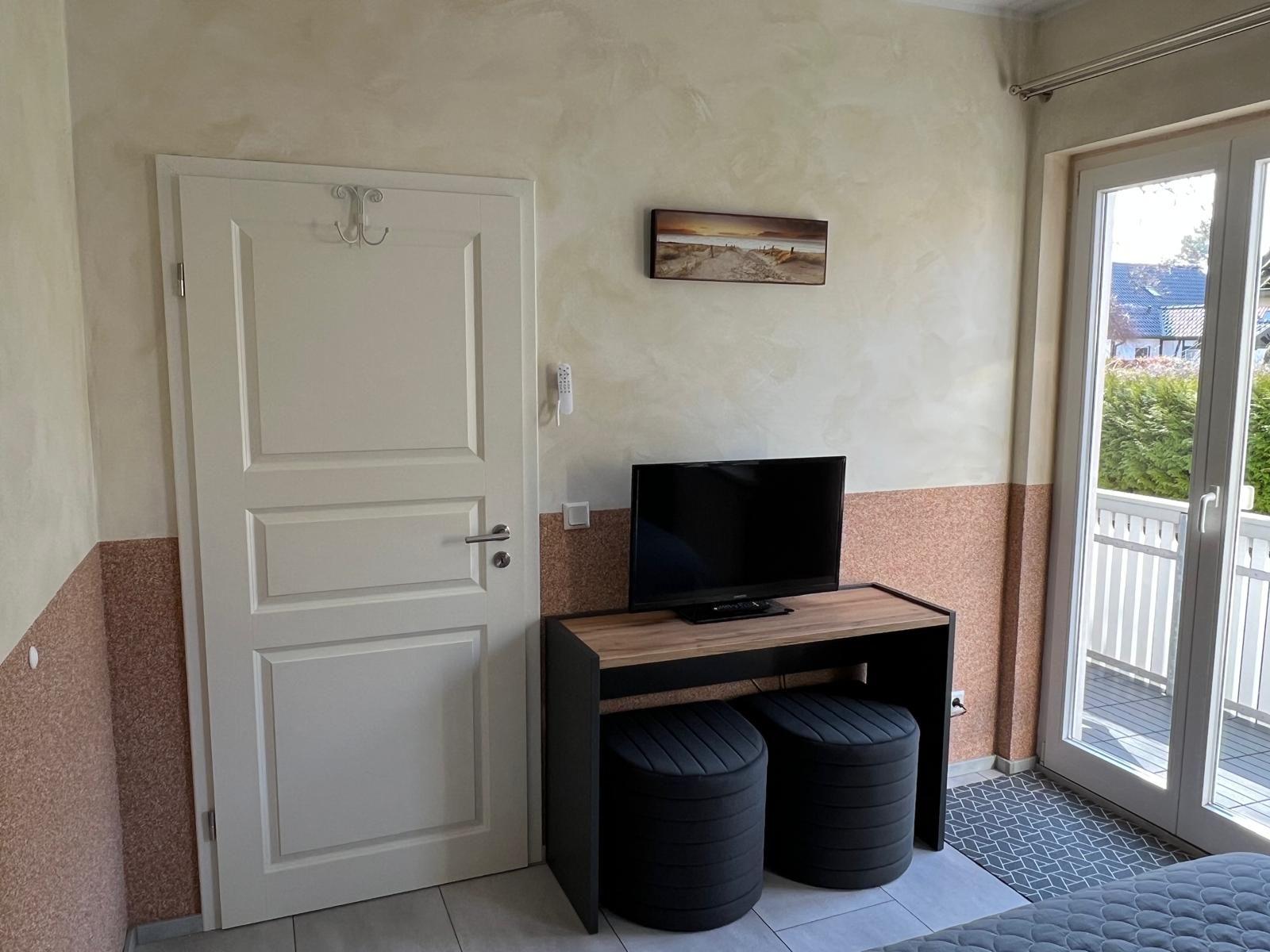 Schlafzimmer mit TV-Tisch, zwei Sitzkissen und Balkontür.