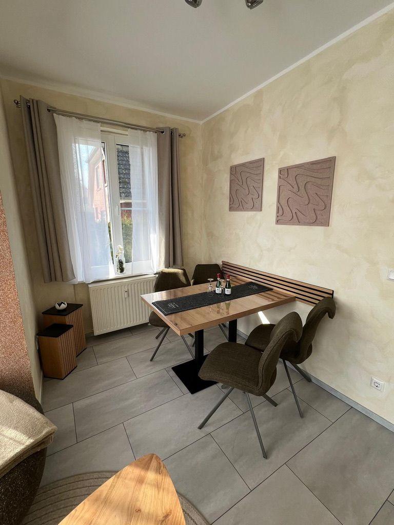 Esszimmer mit Tisch, Stühlen und Fenster. Wanddekoration und Bodenfliesen.