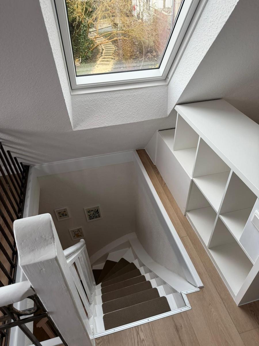 Treppenhaus mit Bücherregal und Dachfenster. Holzfußboden und weiße Wände.