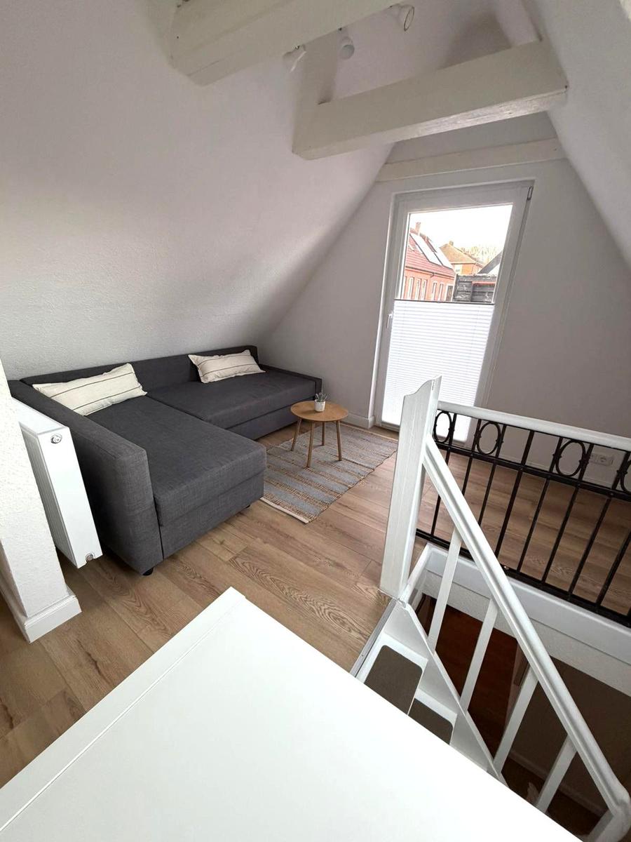 Wohnbereich mit Sofa, Tisch und Balkontür unter Dachschrägen.