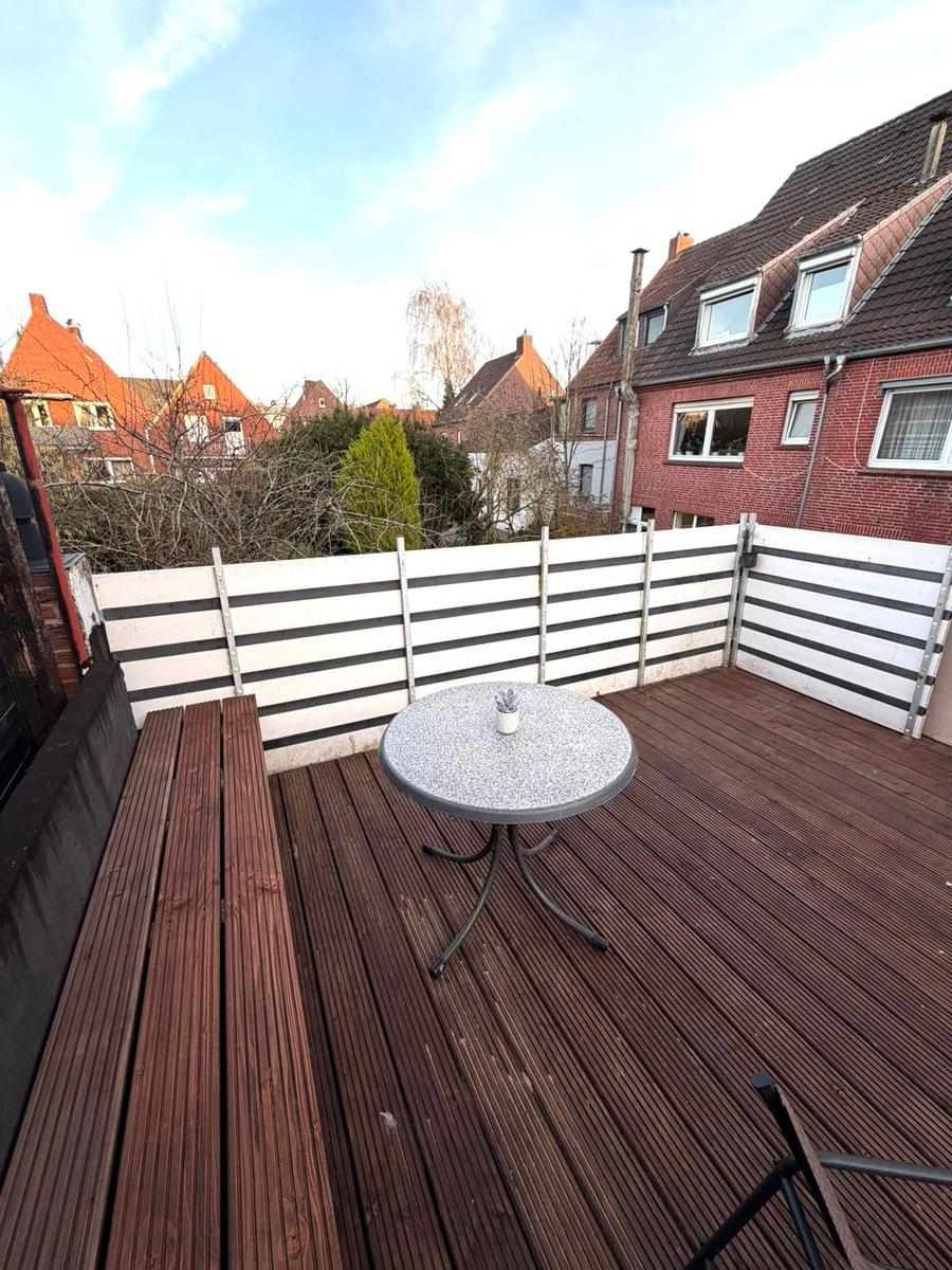 Terrasse mit Holzboden, Tisch und Bank. Blick auf Nachbarhäuser und Bäume.