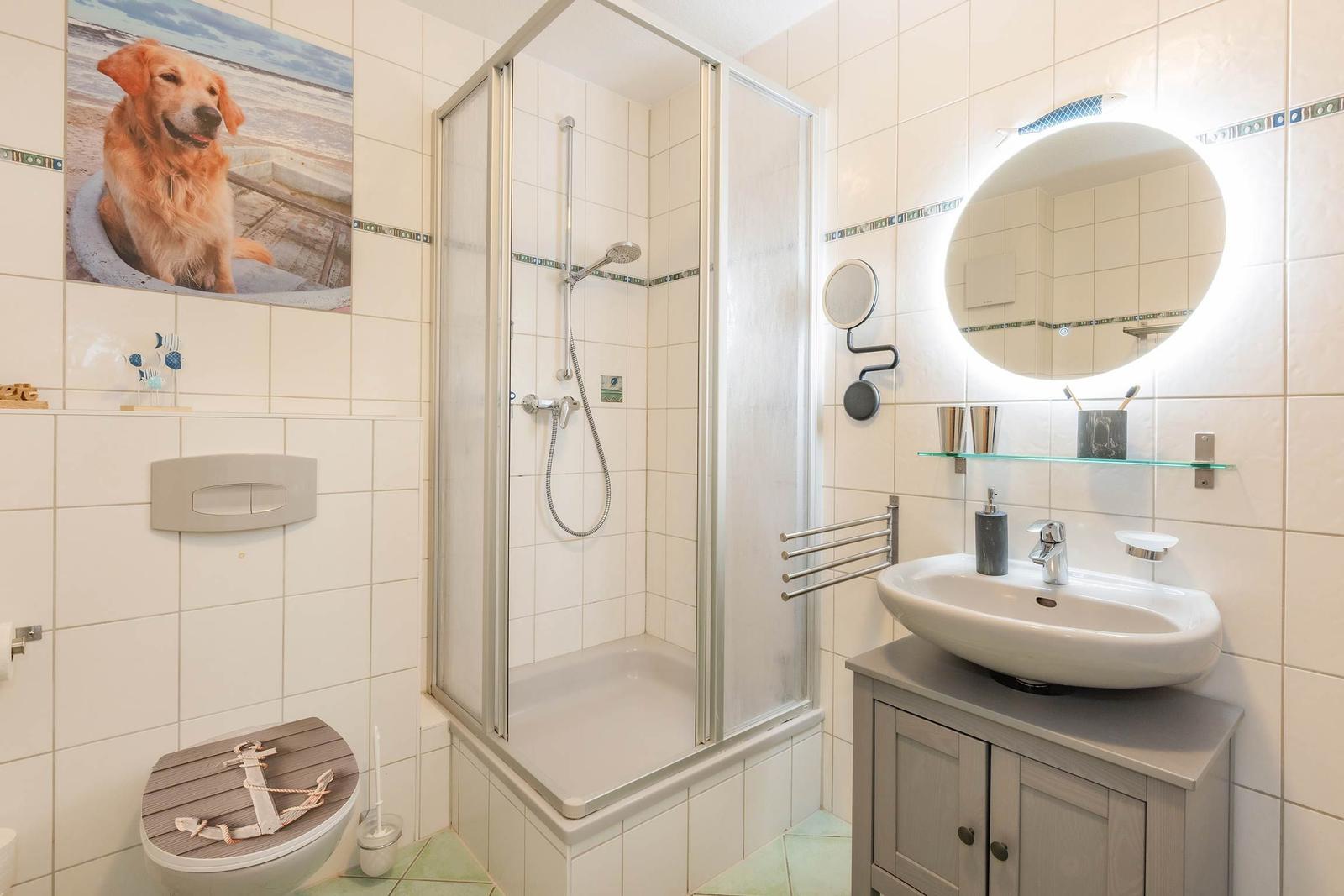 Badezimmer mit Dusche, Waschbecken und Toilette. Wandbild mit Hund.