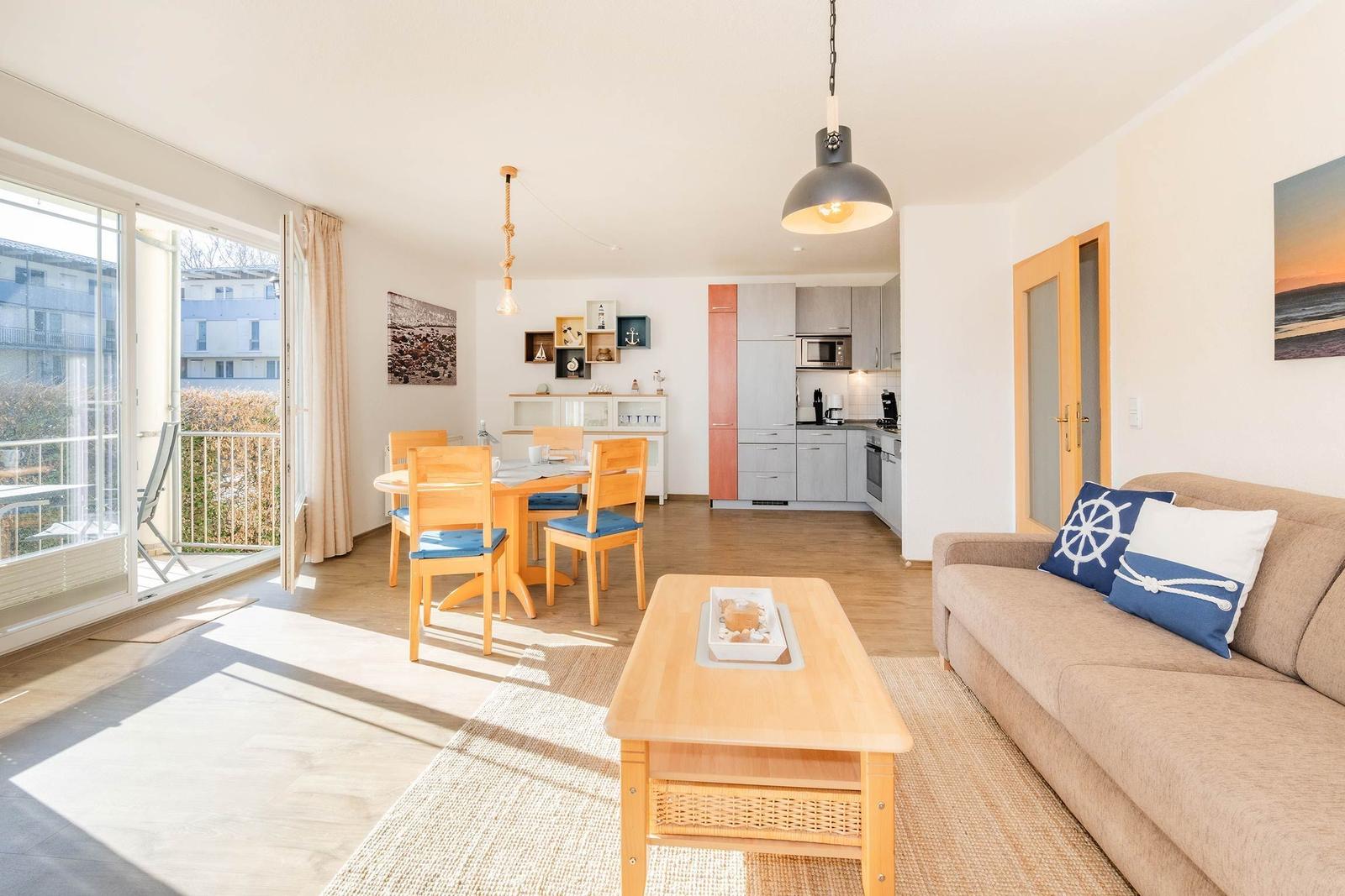Wohn- und Essbereich mit Küche und Balkon. Möbel aus Holz und Sofa mit Kissen.