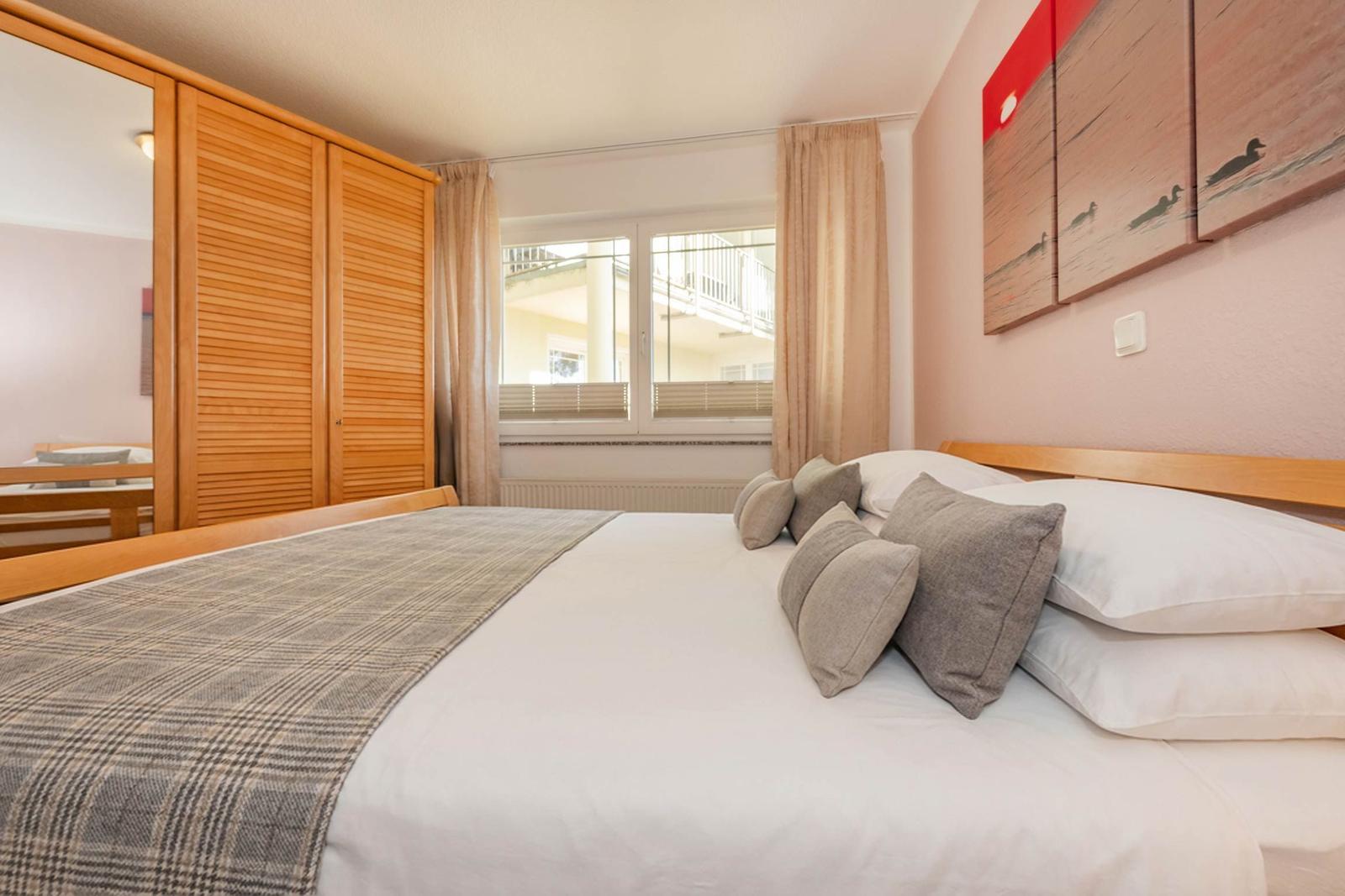 Schlafzimmer mit Bett, Kleiderschrank und Fenster zum Balkon.