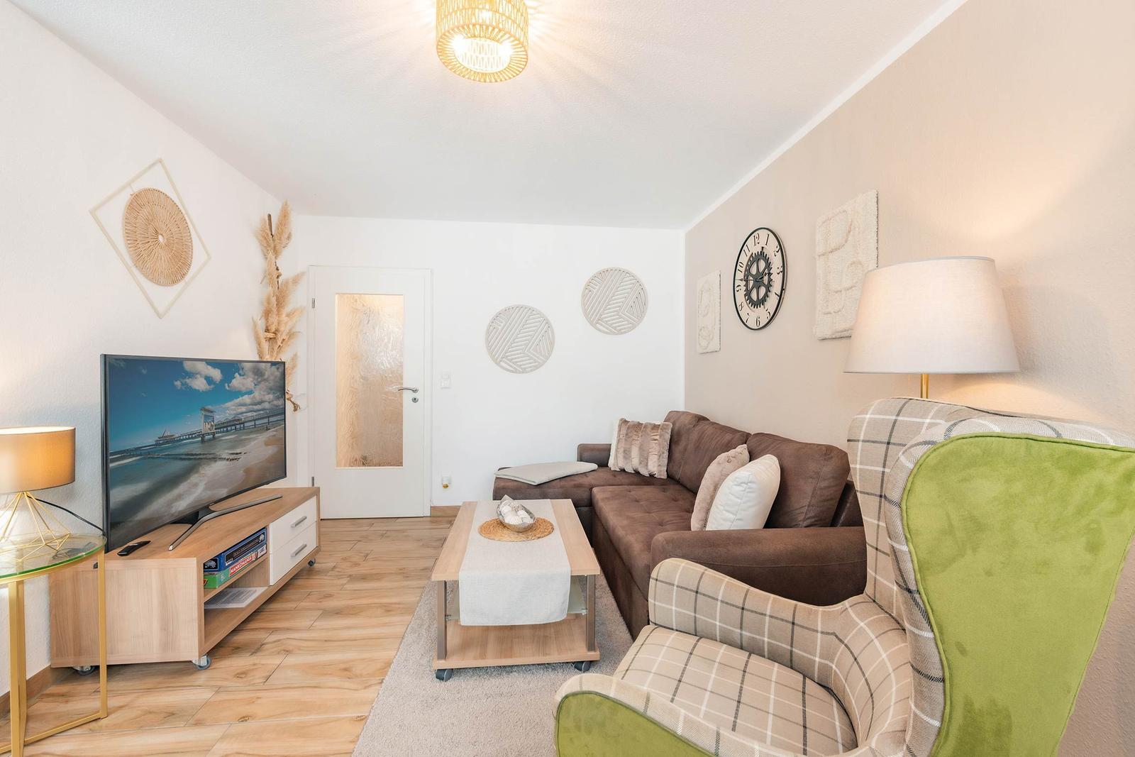 Wohnzimmer mit Sofa, Sessel, Fernseher und Tisch.
