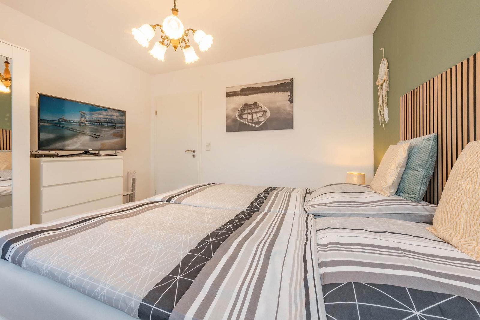 Schlafzimmer mit Doppelbett, Fernseher und Wandbild.