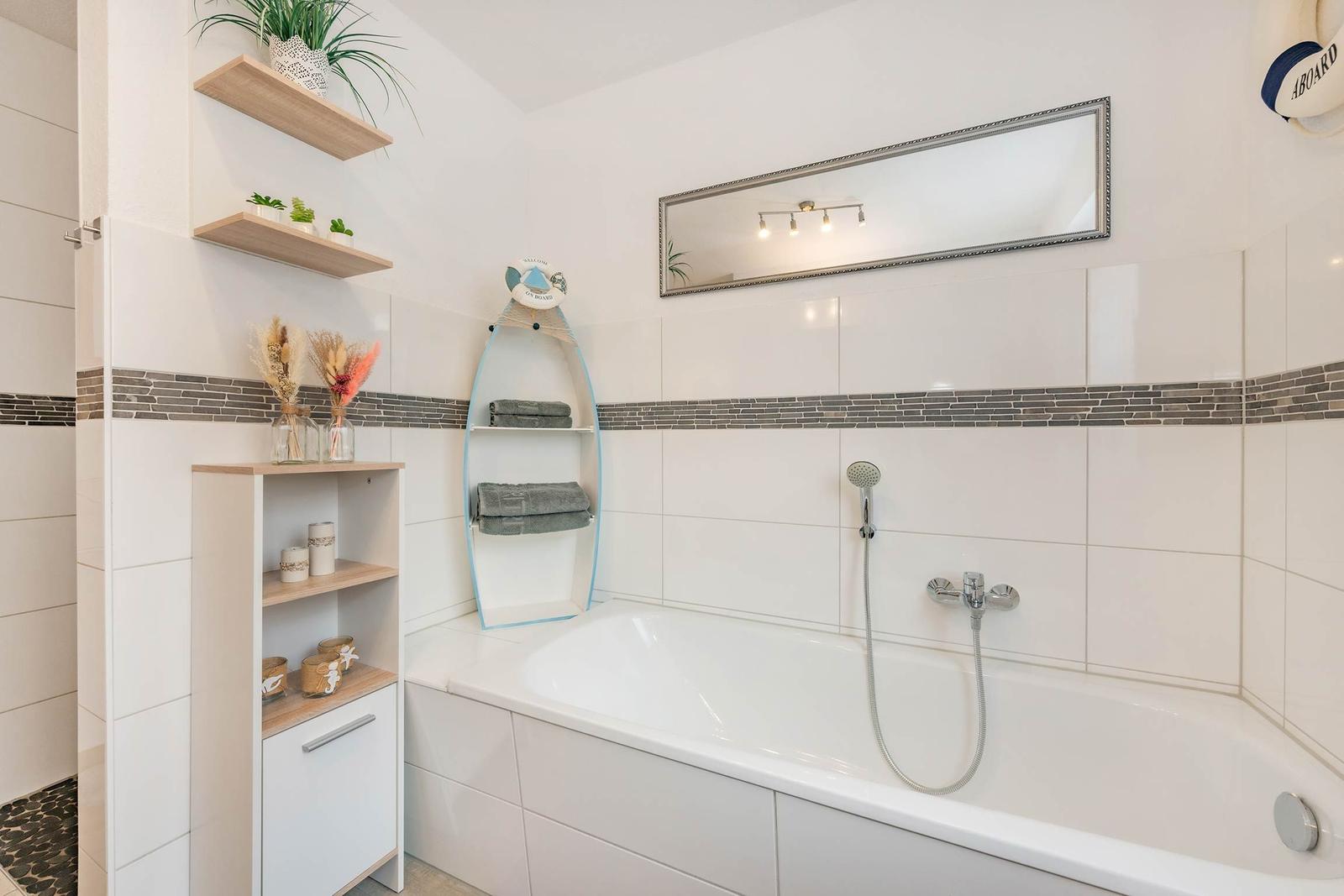 Badezimmer mit Badewanne, Spiegel und Holzregalen. Wandverkleidung mit dunkler Zierleiste.