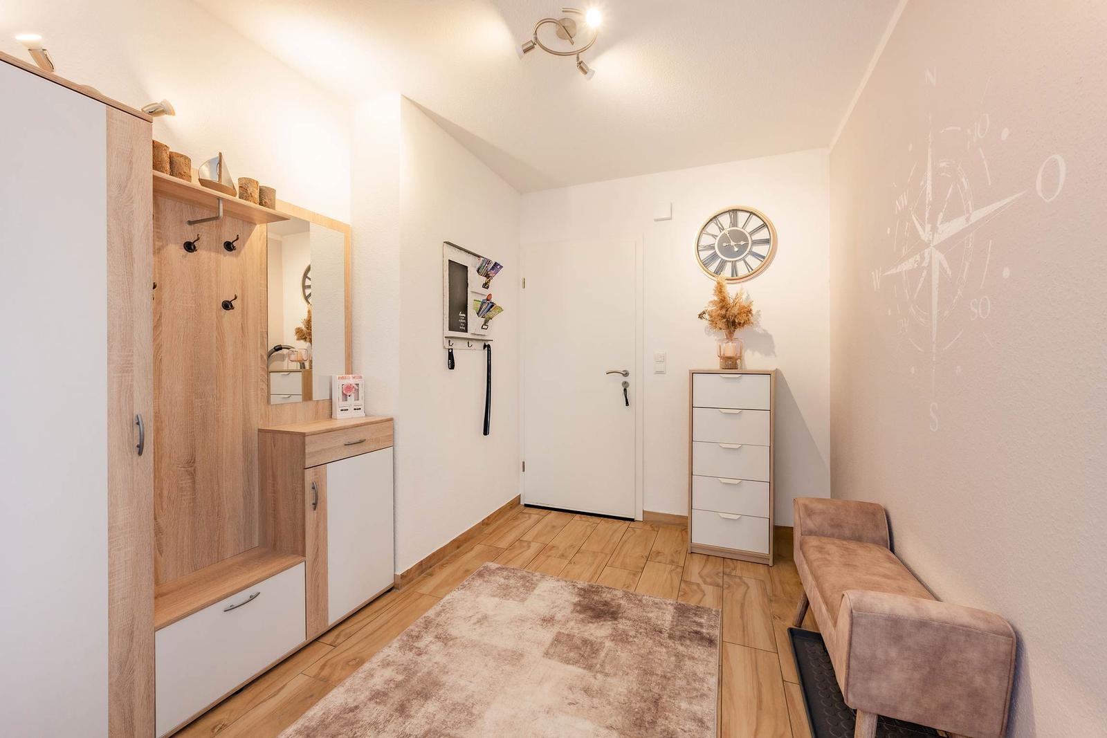 Eingangsbereich mit Kleiderschrank, Sitzbank und Wanduhr.