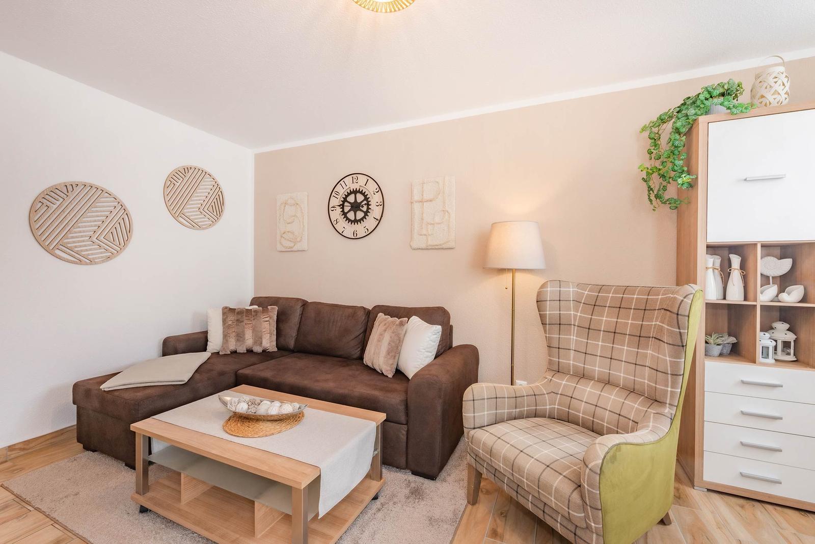 Wohnzimmer mit Sofa, Sessel und Tisch. Wanddekoration und Beleuchtung sichtbar.