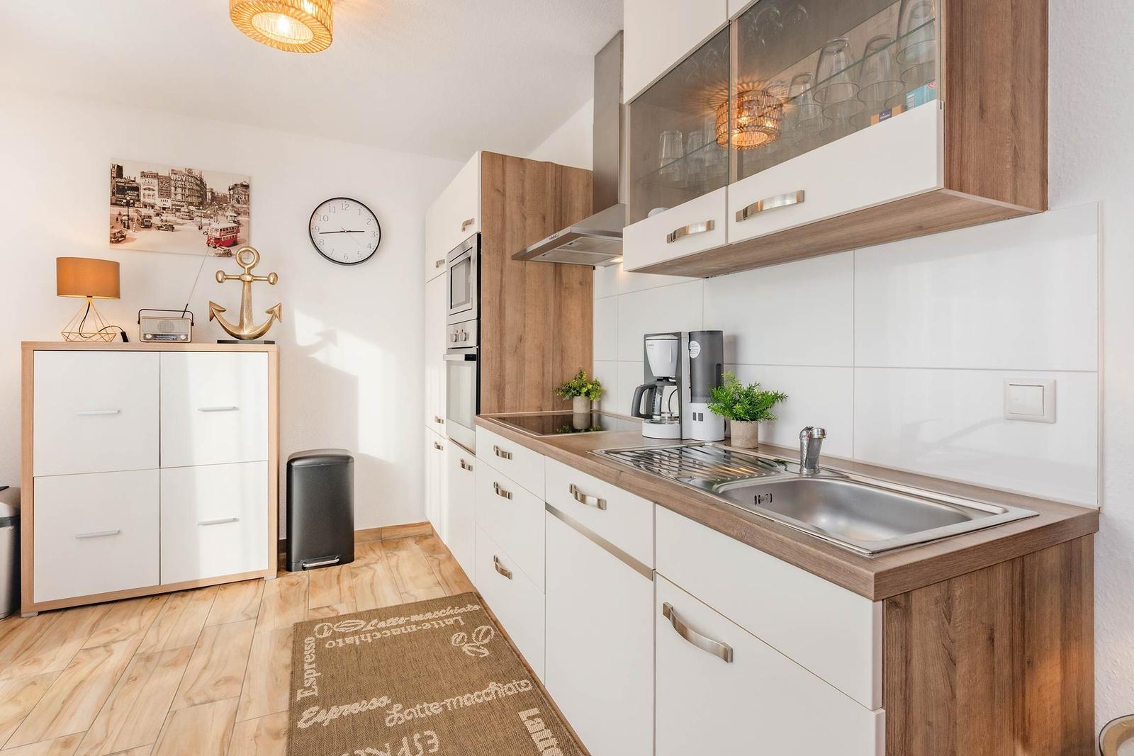 Küche mit Holz- und weißen Schränken, Spüle, Kaffeemaschine und Wanduhr.