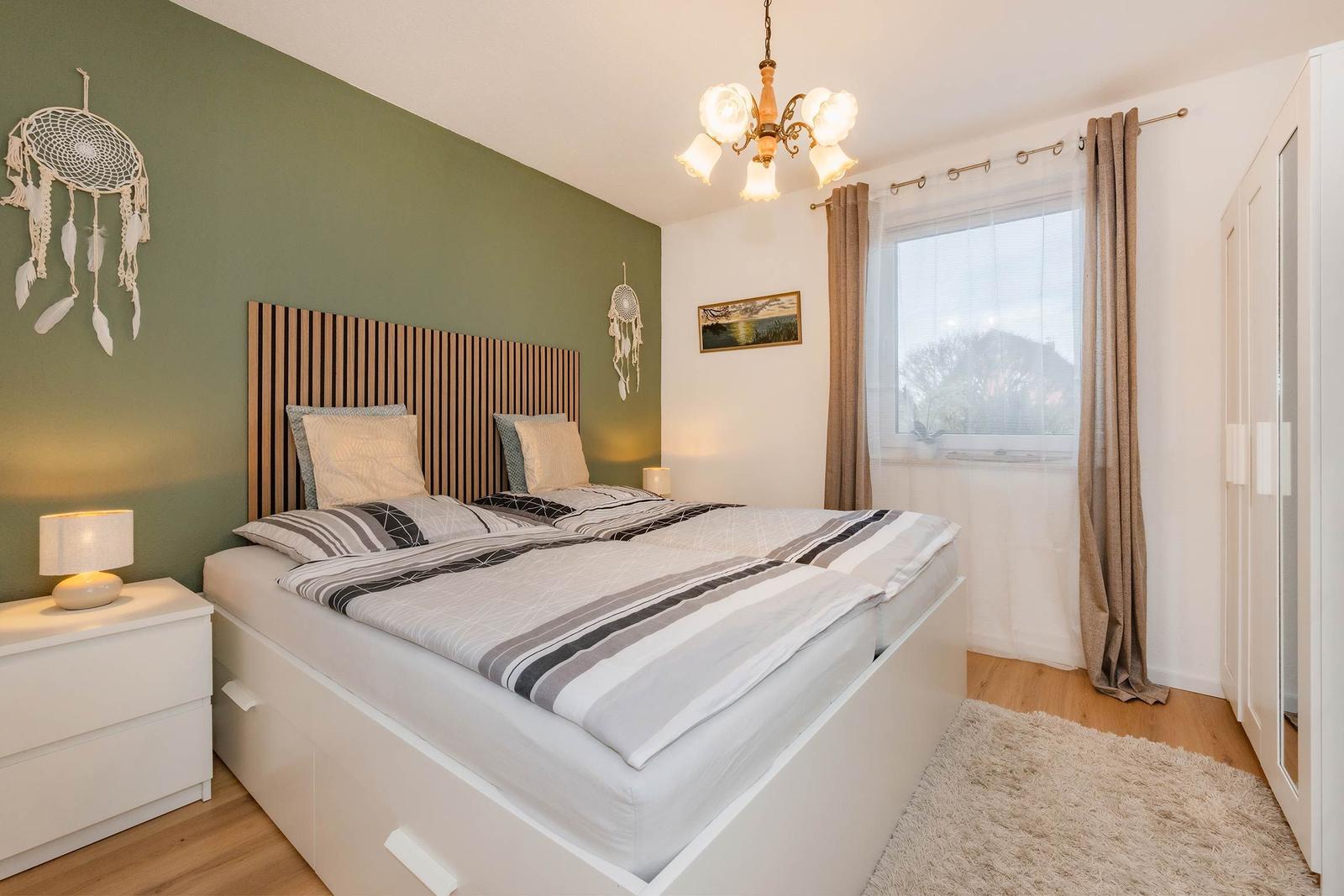 Schlafzimmer mit Doppelbett, grüner Wand und Fenster mit Vorhängen.