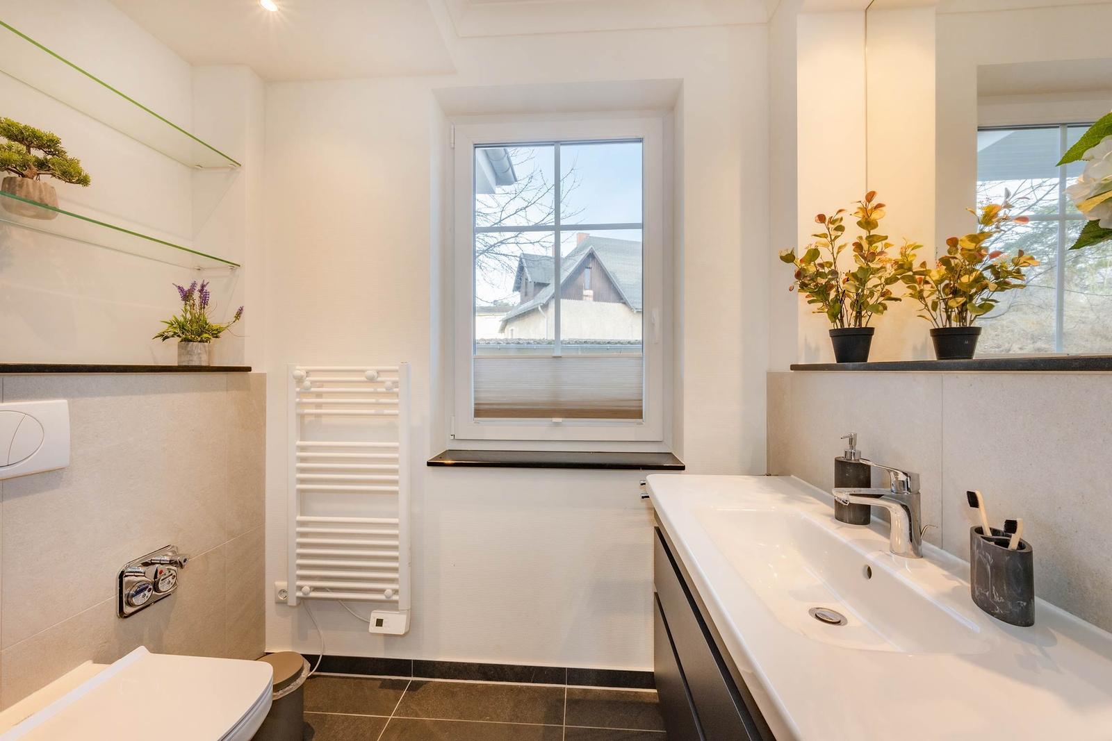 Badezimmer mit Waschbecken, Toilette und Fenster. Pflanzen auf der Fensterbank.