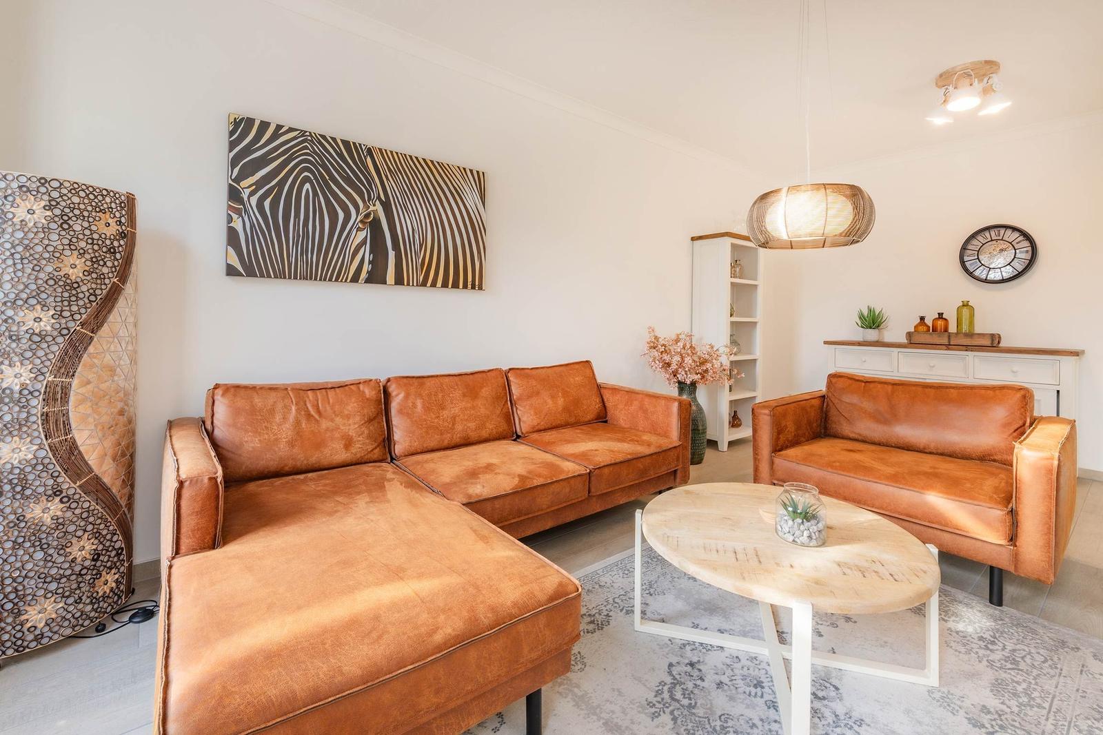Wohnzimmer mit braunen Ledersofas, runden Tisch und Wandbild mit Zebra-Muster.