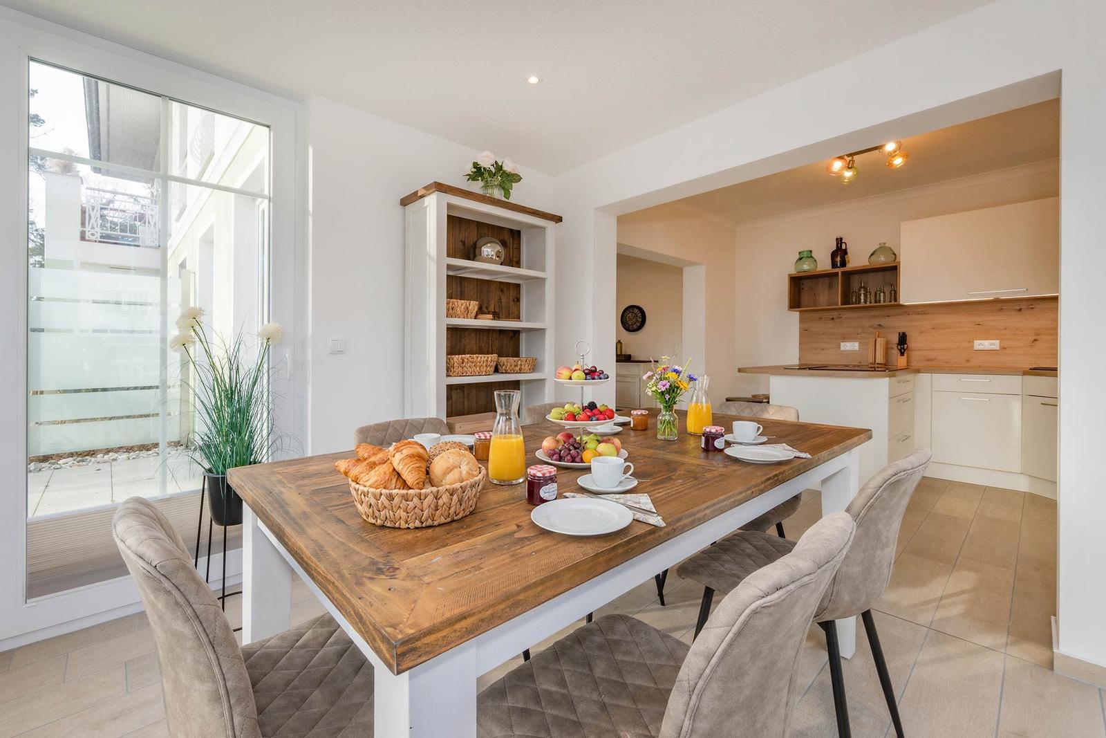 Essbereich mit Holztisch, Stühlen und Obstfrüchten. Küche im Hintergrund.