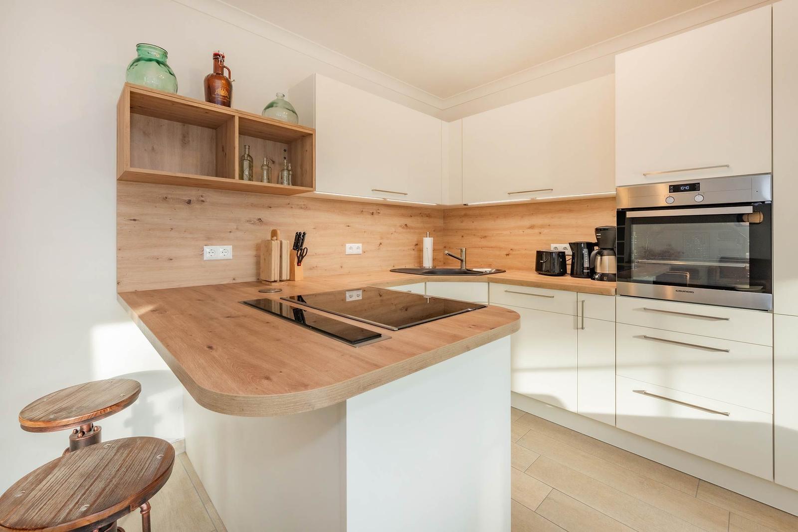 Moderne Küche mit Holz Arbeitsfläche und weißen Schränken. Einbauherd und Backofen sind vorhanden.