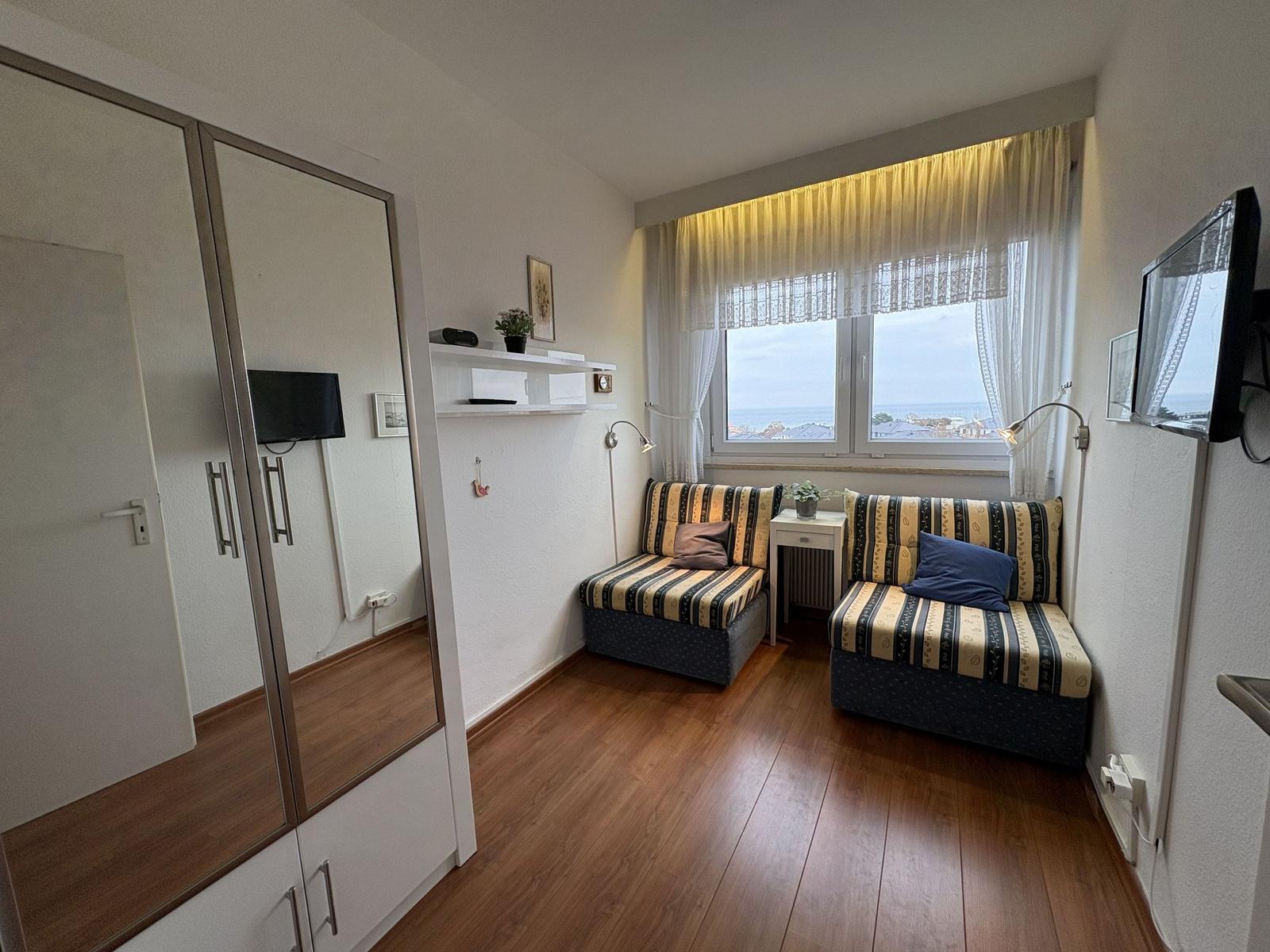 Zimmer mit zwei Sitzbänken, Fenster mit Meerblick und Spiegelschrank.