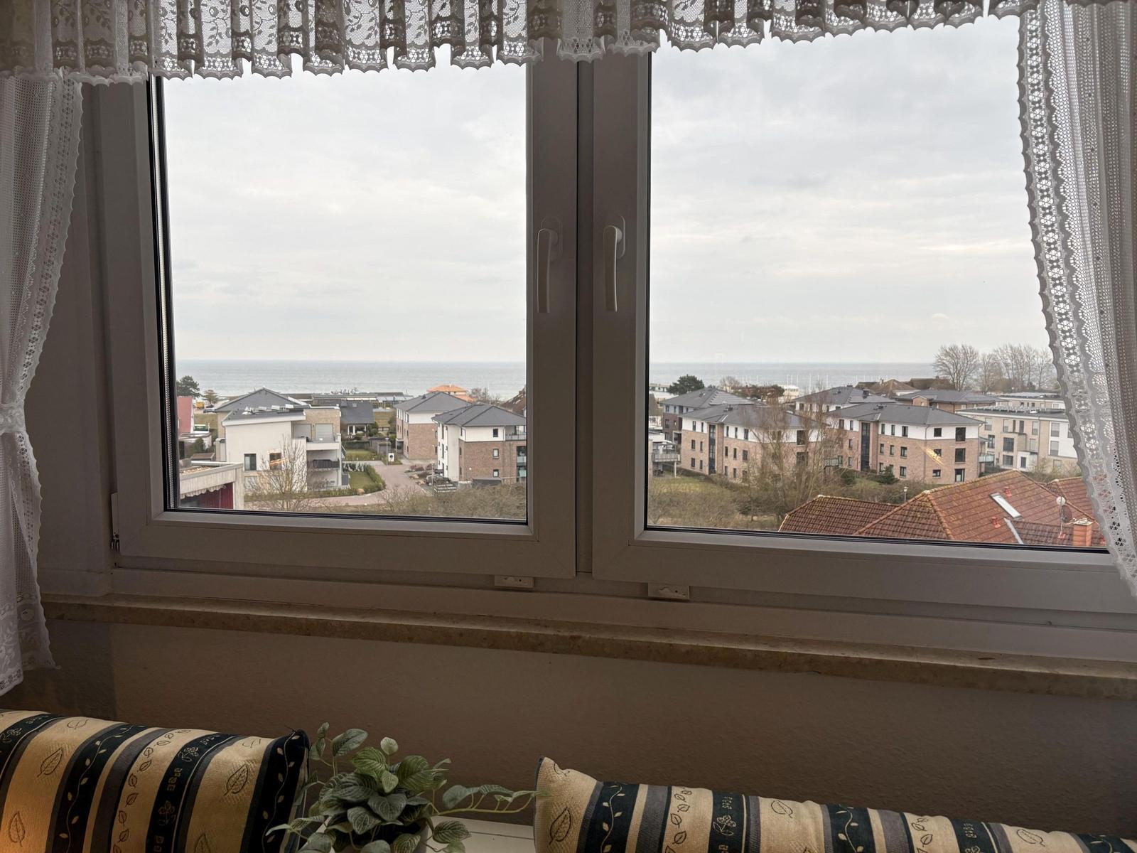 Durch das Fenster blickt man auf das Meer und Wohnhäuser.