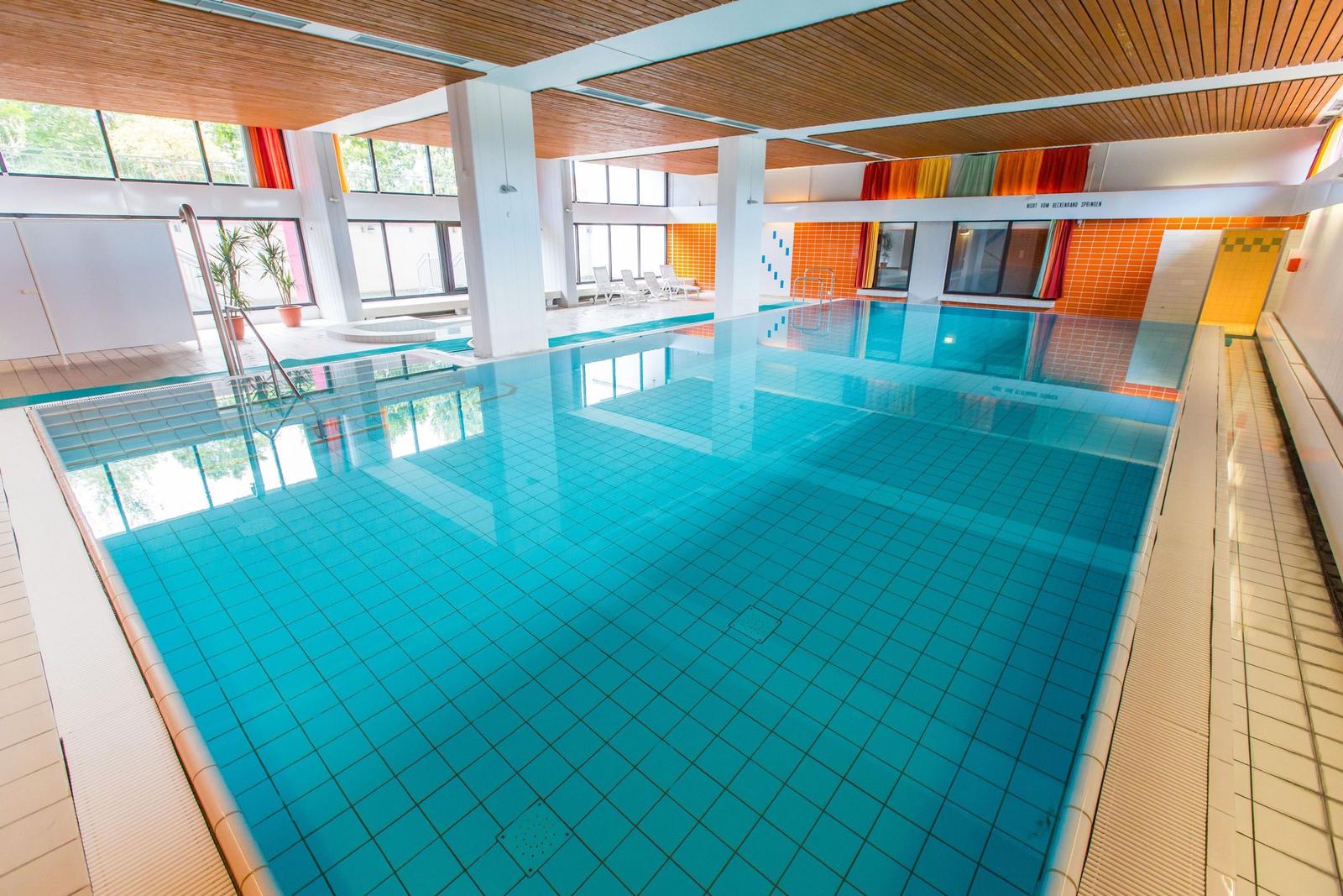 Großes Hallenbad mit blauem Wasser und Holzdecke.