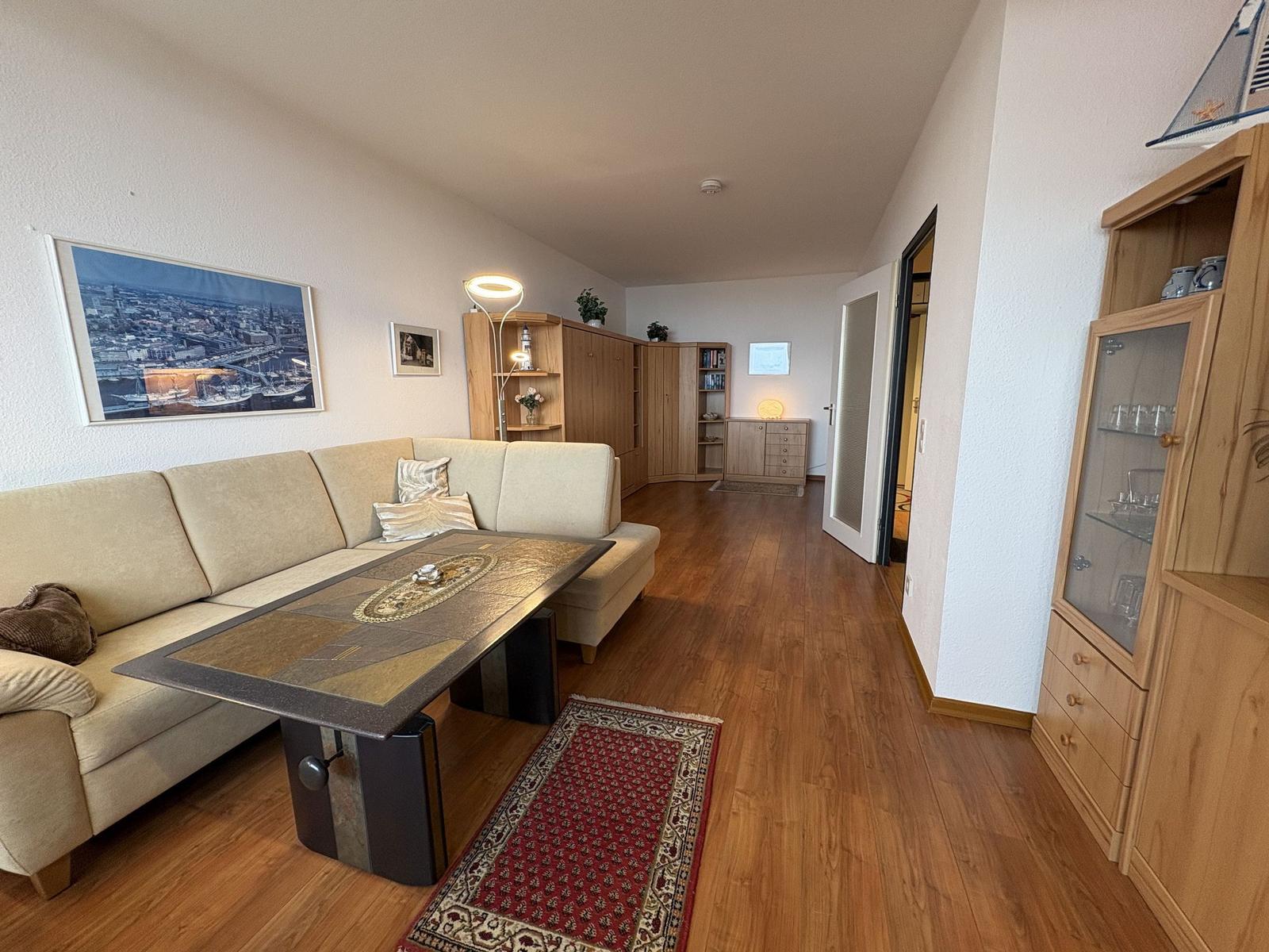 Wohnzimmer mit Sofa, Tisch und Holzboden. Regal und Schrank sind sichtbar.