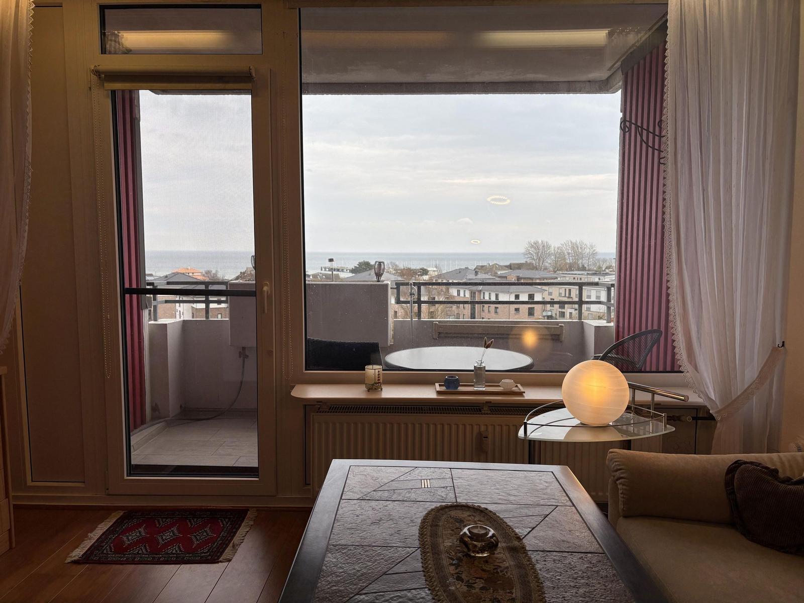 Wohnraum mit Blick auf das Meer und Balkon mit Tisch und Stühlen.