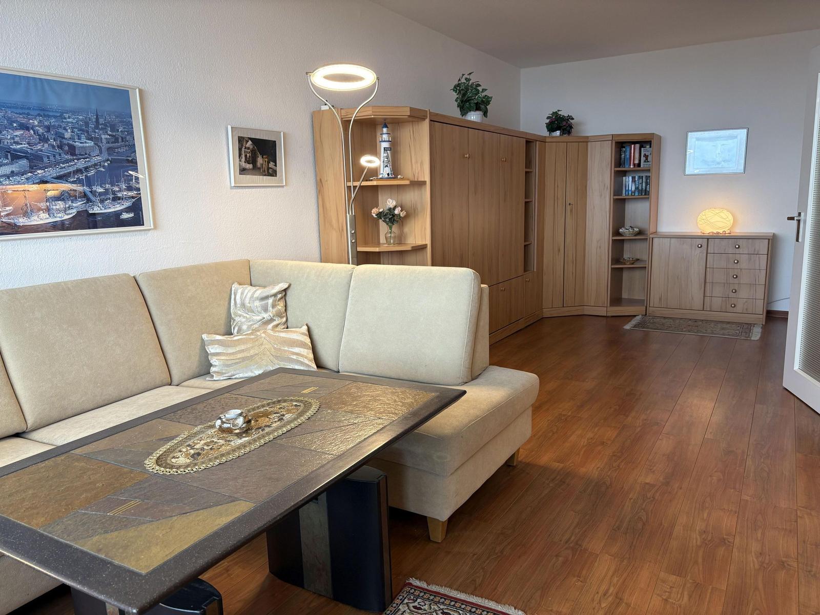 Wohnzimmer mit Sofa, Tisch und Holzmöbeln. Wandbild und Beleuchtung sichtbar.