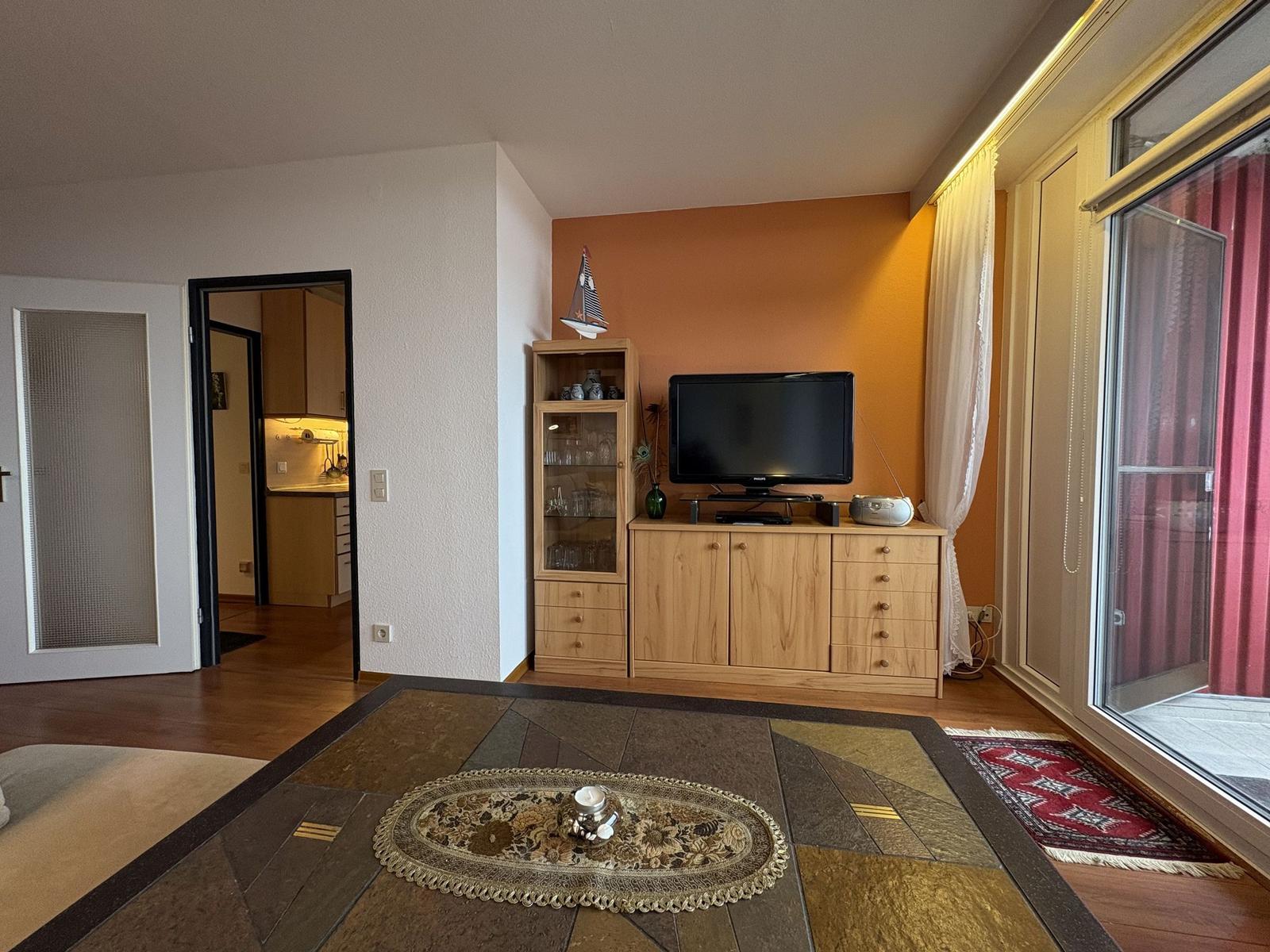 Wohnzimmer mit Holzmöbeln, Fernseher und Blick auf Balkon