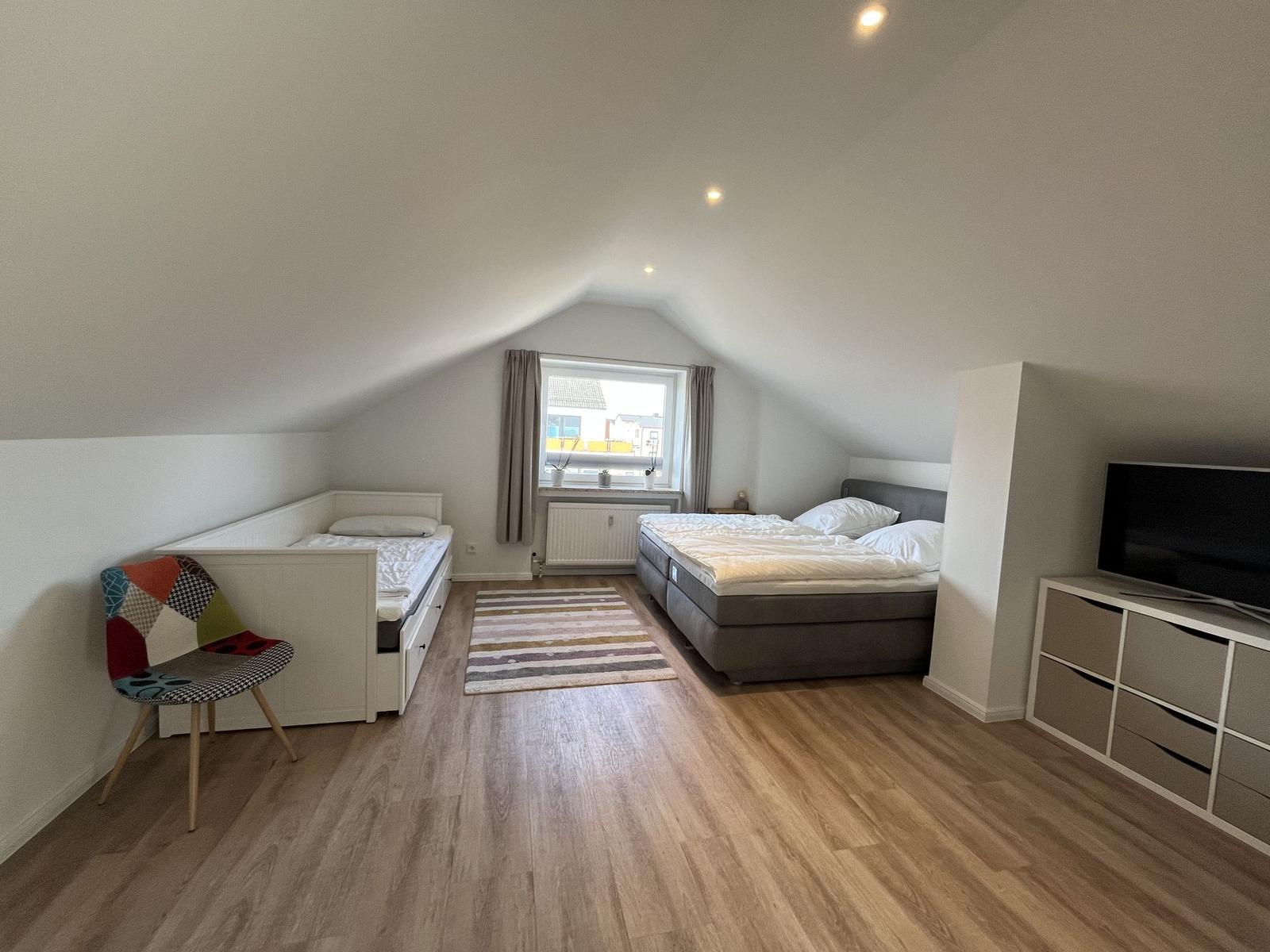 Schlafzimmer mit Dachschräge, Bett, kleiner Schlafcouch und Fernseher.