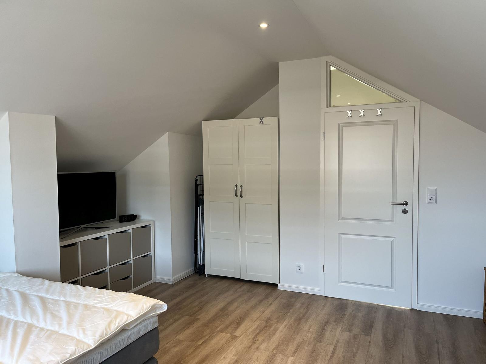 Schlafzimmer mit Dachschräge, Bett, Kleiderschrank und TV-Bereich.