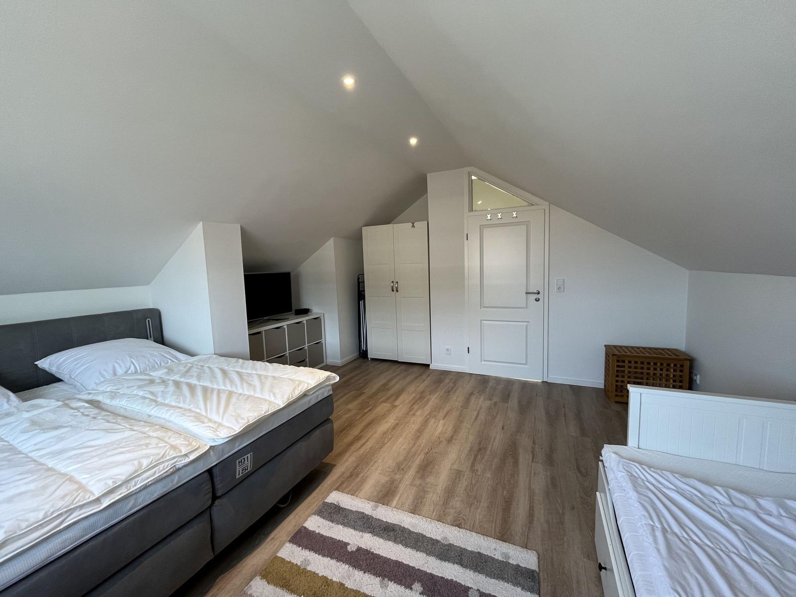 Schlafzimmer mit Doppelbett, Kinderbett und Holzboden unter schrägen Dachschrägen.