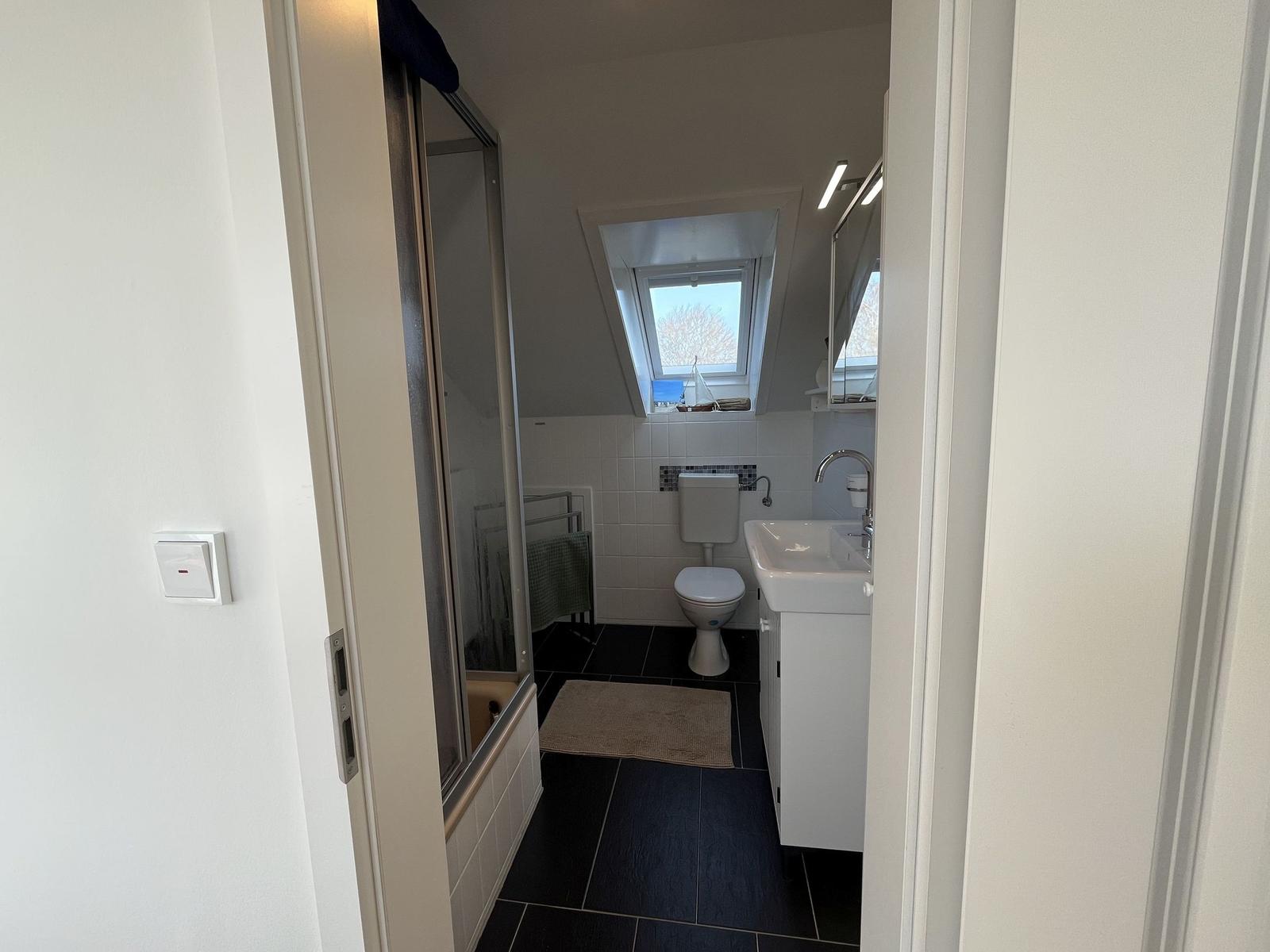 Badezimmer mit Dusche, Toilette und Waschbecken unter Dachschrägen.