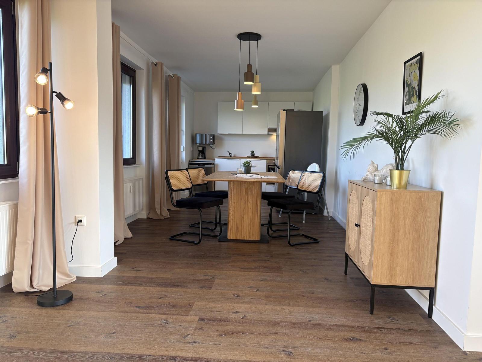 Essbereich mit Tisch, Stühlen und Küchenbereich im Hintergrund.