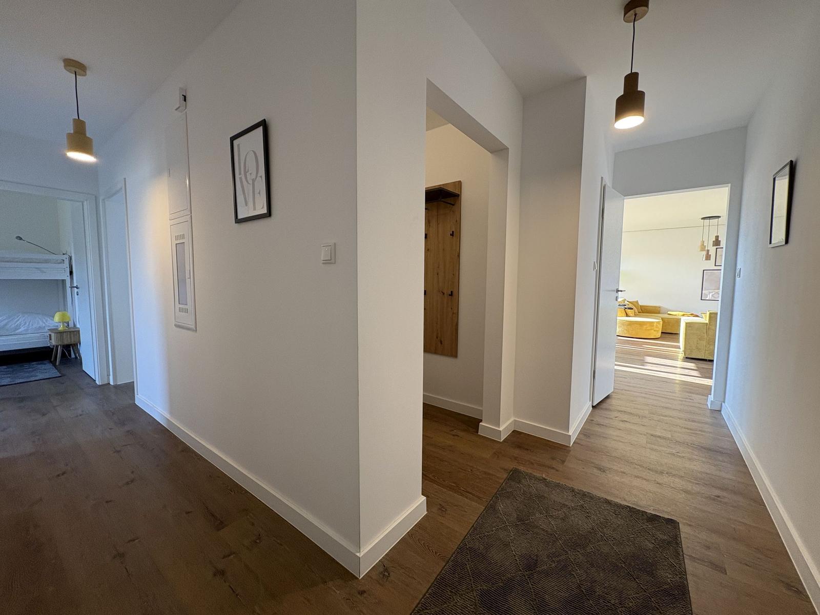 Flur mit Holzboden, Wandbild und Blick in Schlaf- und Wohnbereich.