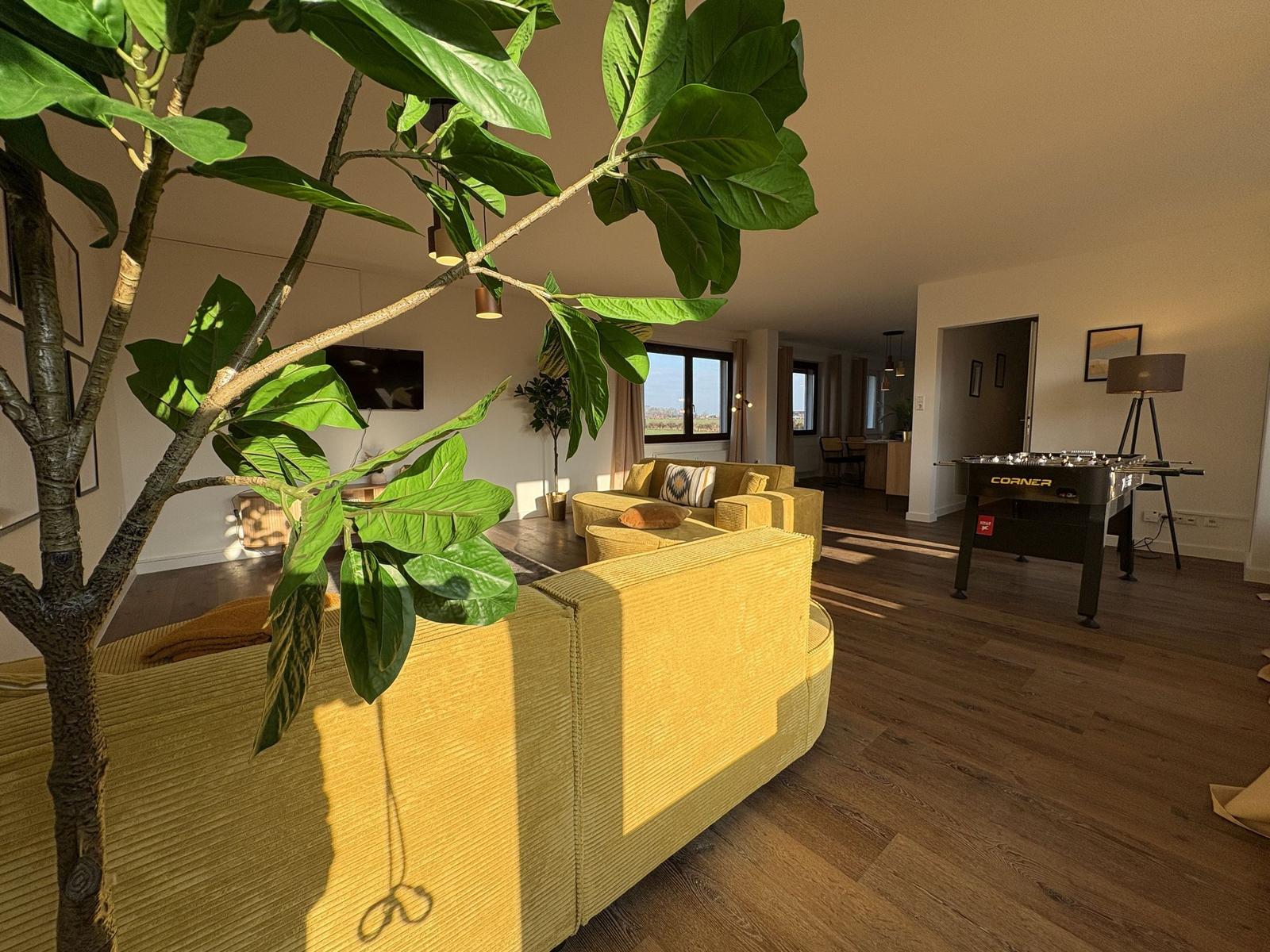 Wohnzimmer mit gelben Sitzmöbeln, Holzboden und Fußballtisch.