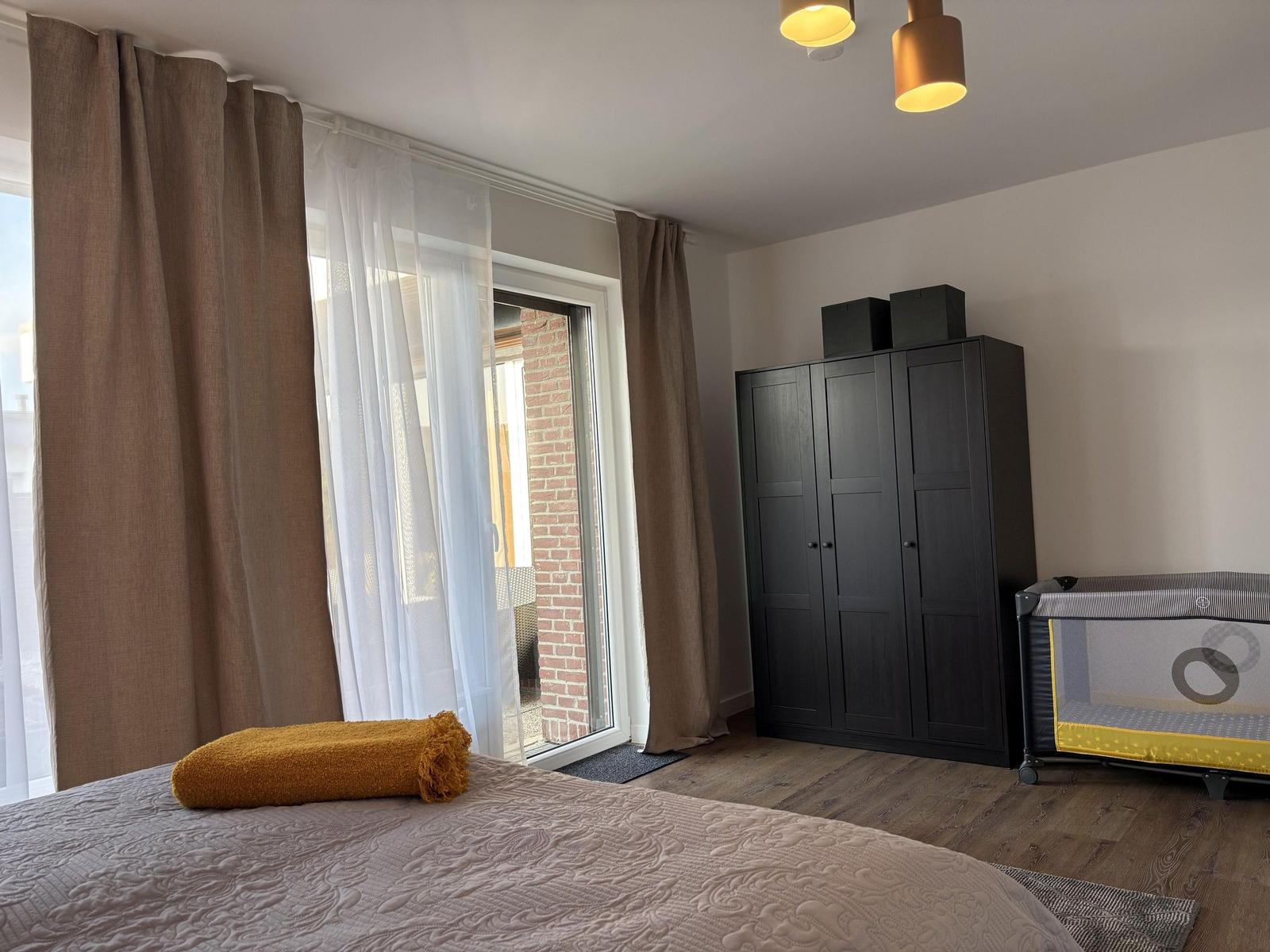 Schlafzimmer mit Bett, Kleiderschrank und Babybett. Fenster mit Vorhängen.