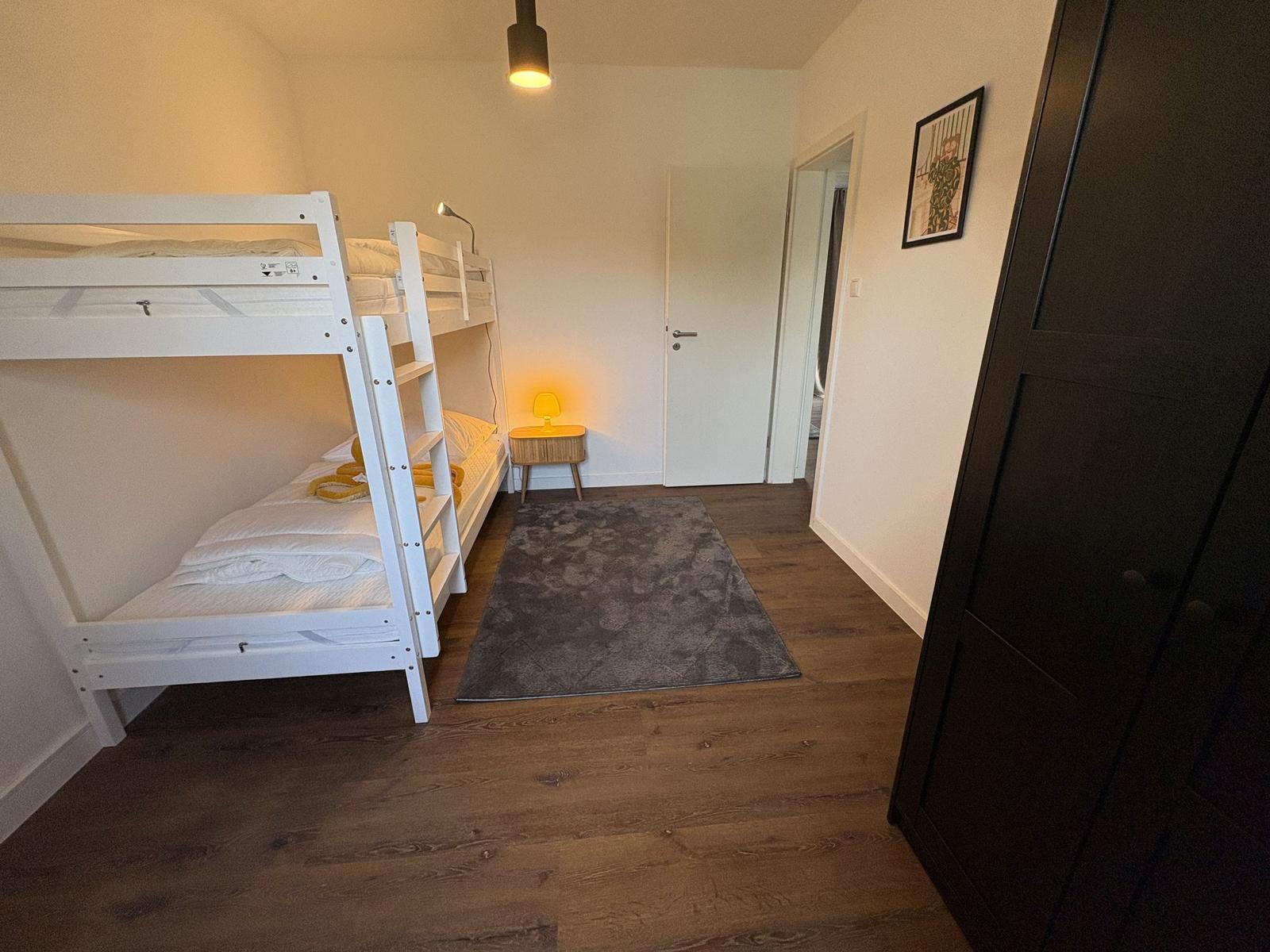 Zimmer mit Doppelstockbett, Teppich und Nachttisch mit Lampe.